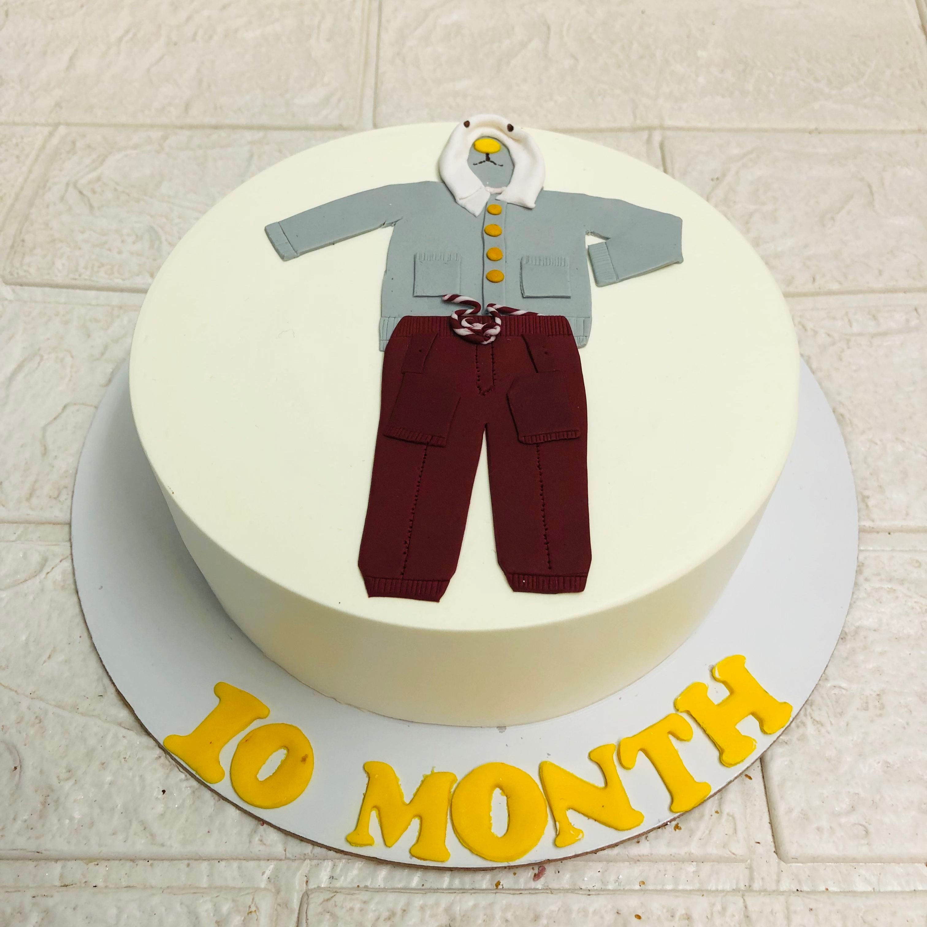 A delightful cake featuring a charming baby outfit, ideal for commemorating a new arrival.