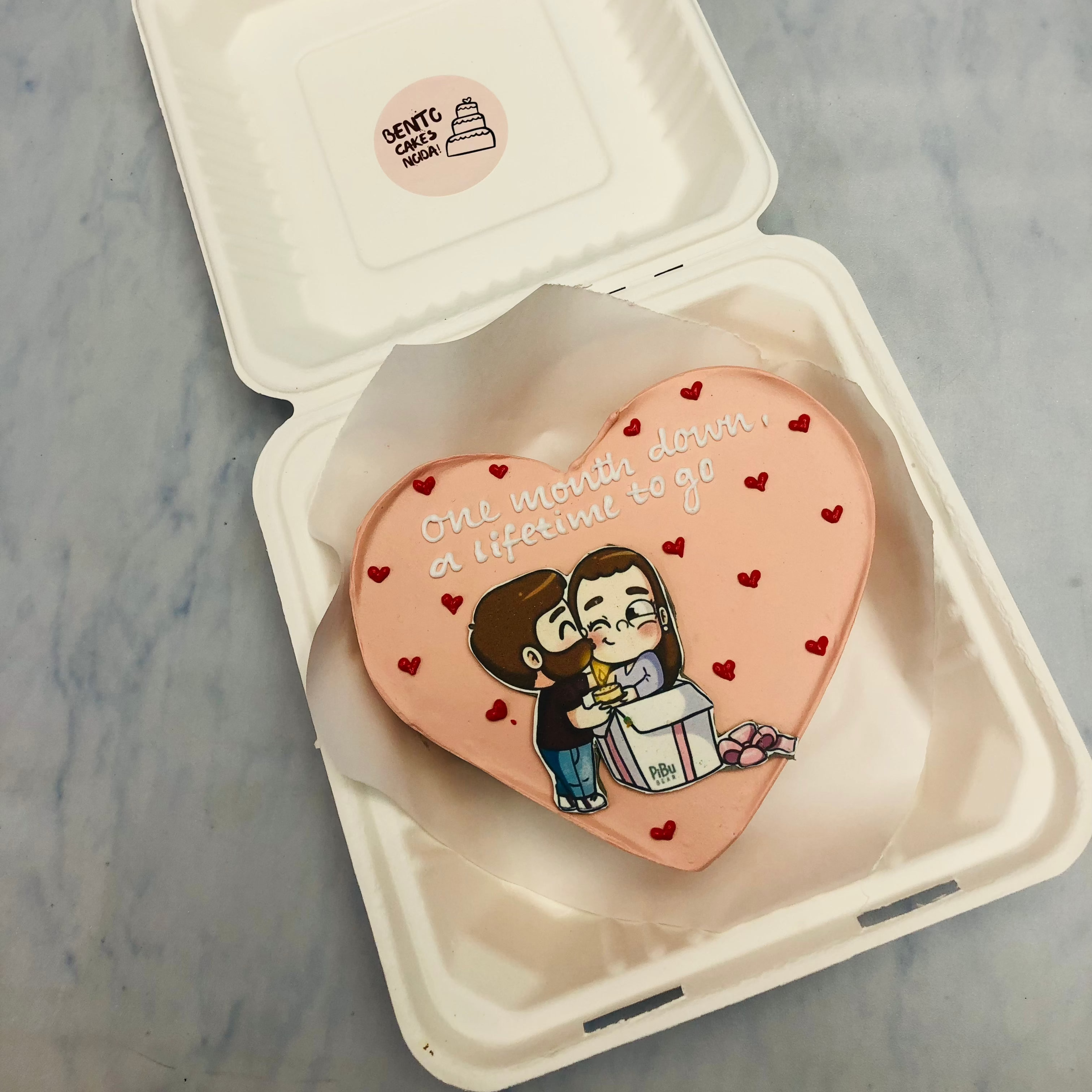 A peach color heart shape cake with a kissing couple print and filled with red hearts.