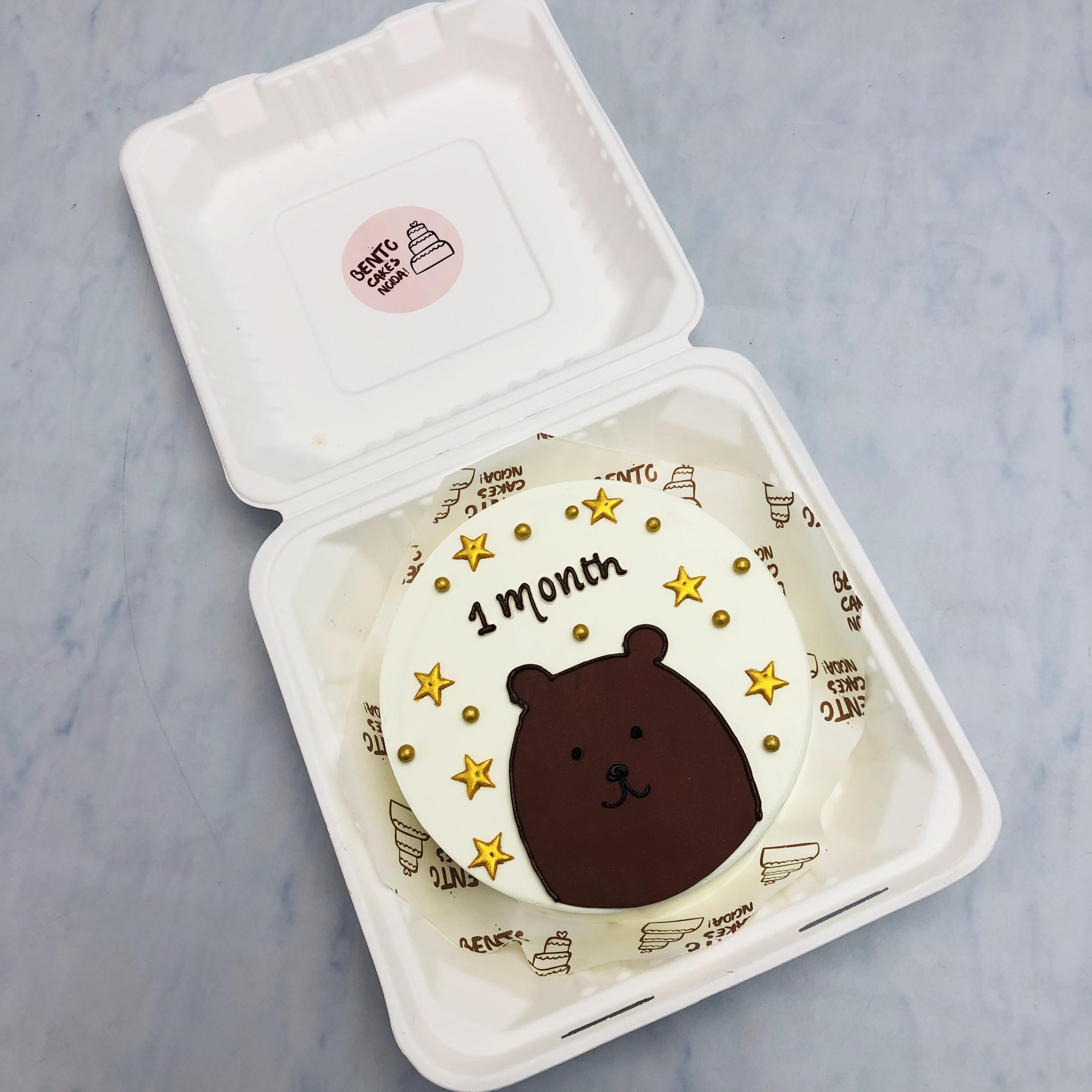 A white bento cake with a brown bear face design, cake filled with golden stars.