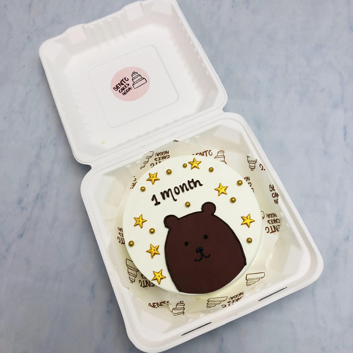 A white bento cake with a brown bear face design, cake filled with golden stars.
