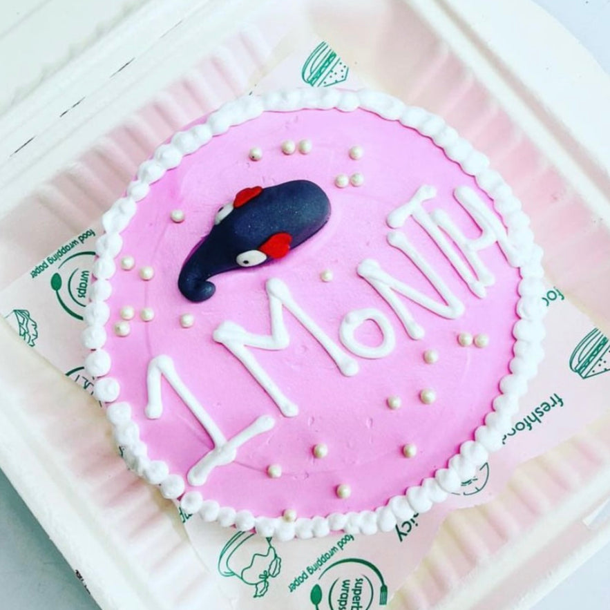 A pink cake in a soft foam container, adorned with the inscription "month 1" on top, celebrating a special milestone.