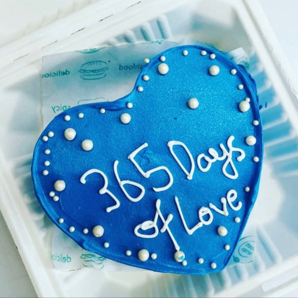 A heart-shaped cake in blue, featuring the inscription "365 days of love" beautifully displayed on top.