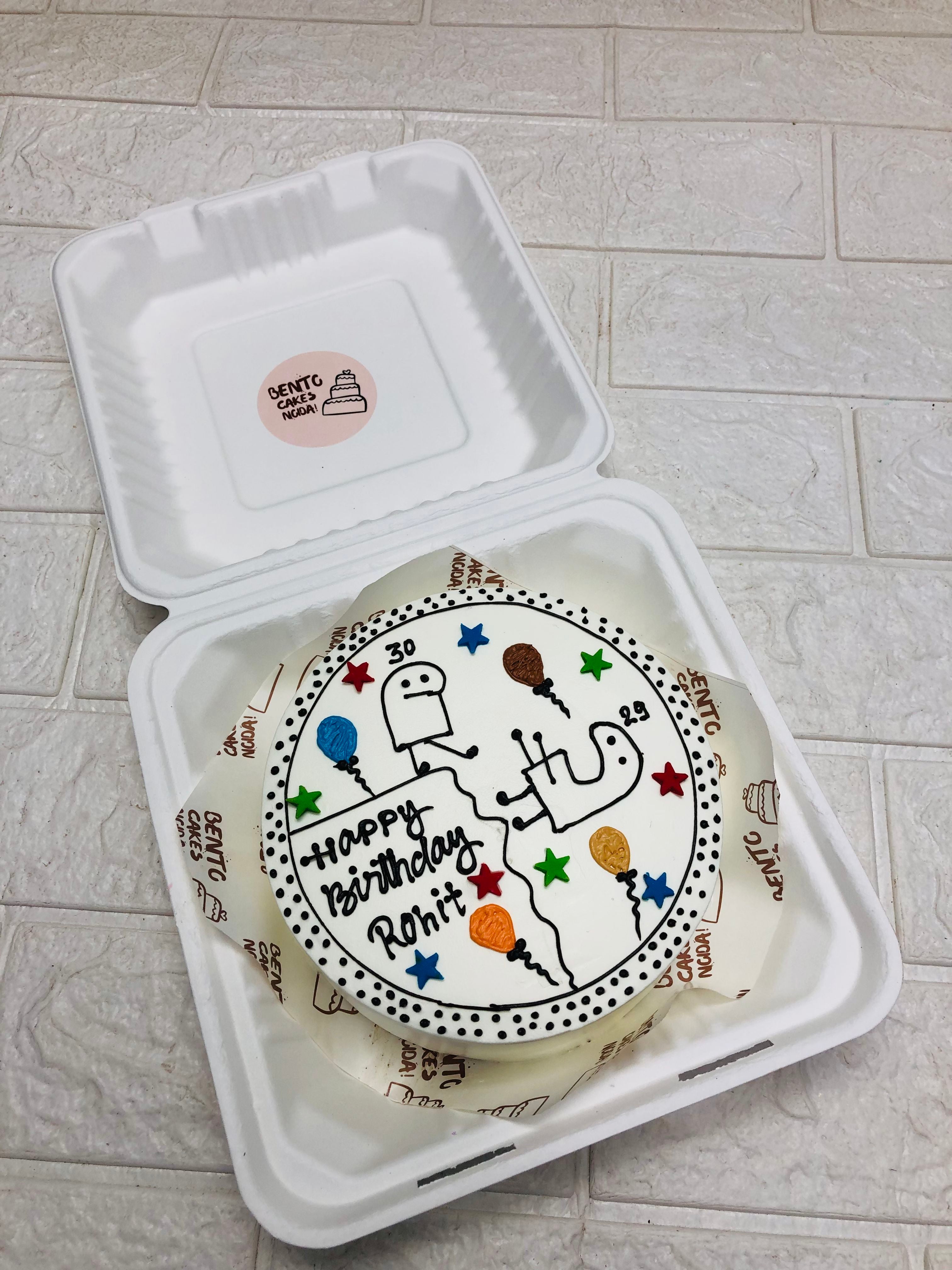 A white bento cake with colorful doodles of stick figures holding balloons and stars, featuring the message "Happy Birthday Rohit" in black icing, inside a bento box.