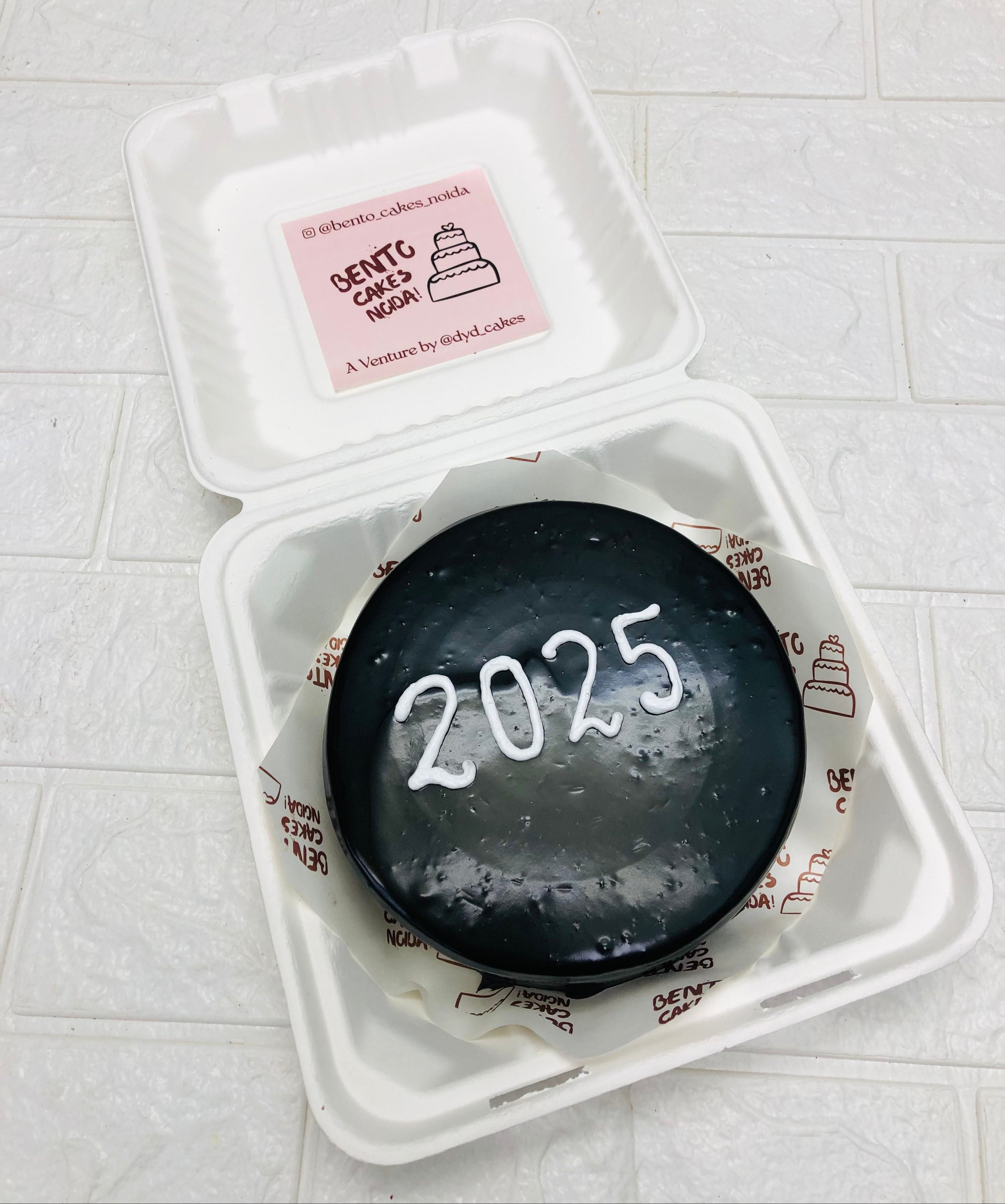 A black chocolate cake in a bento box with a 2025 written with white color for new year special occasion.