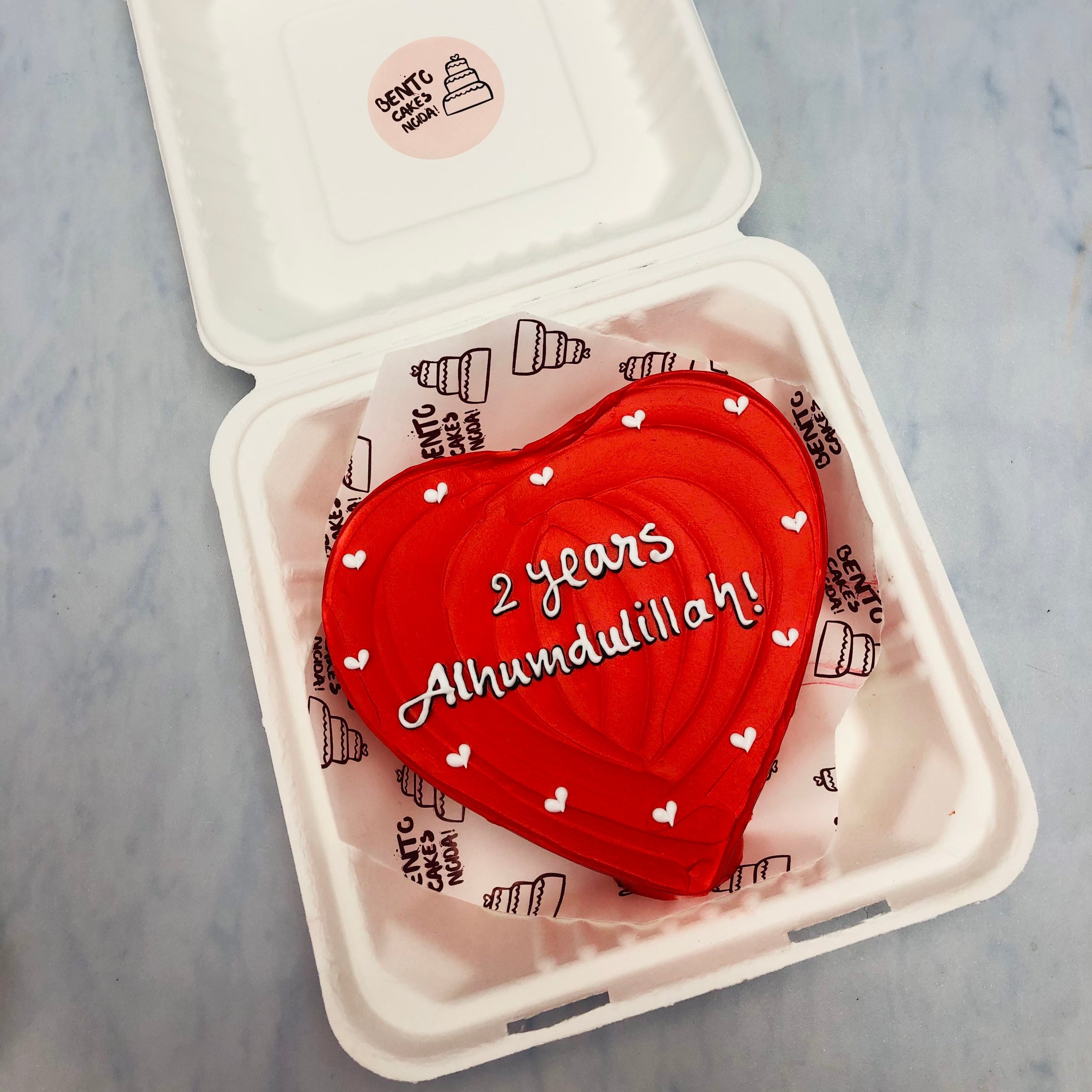 A red icing heart shape cake with waivy design on top and white little hearts made on its boundary.