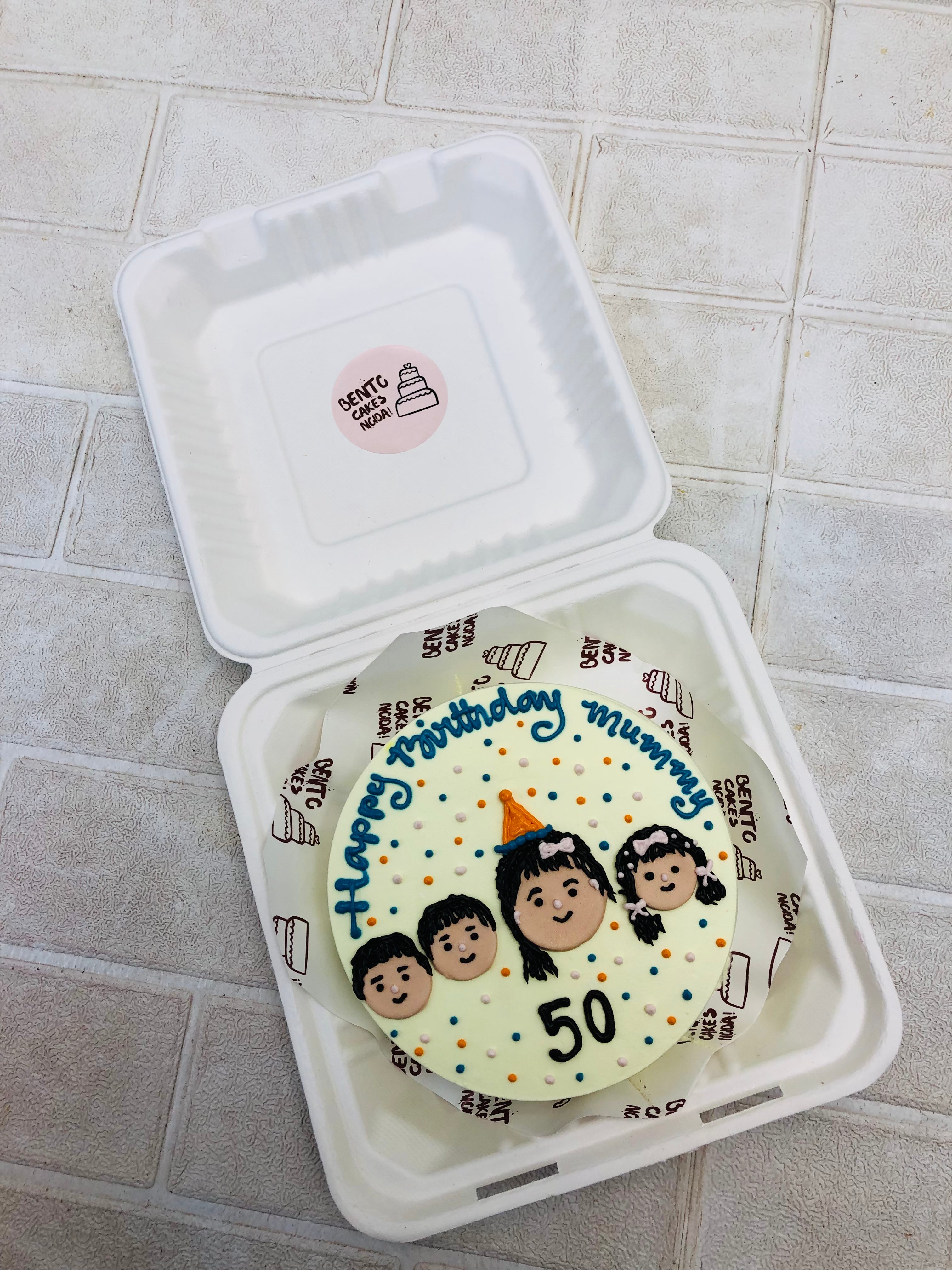 An off white bento cake in which a mom and 3 childs faces, celebrating her mothers birthday.