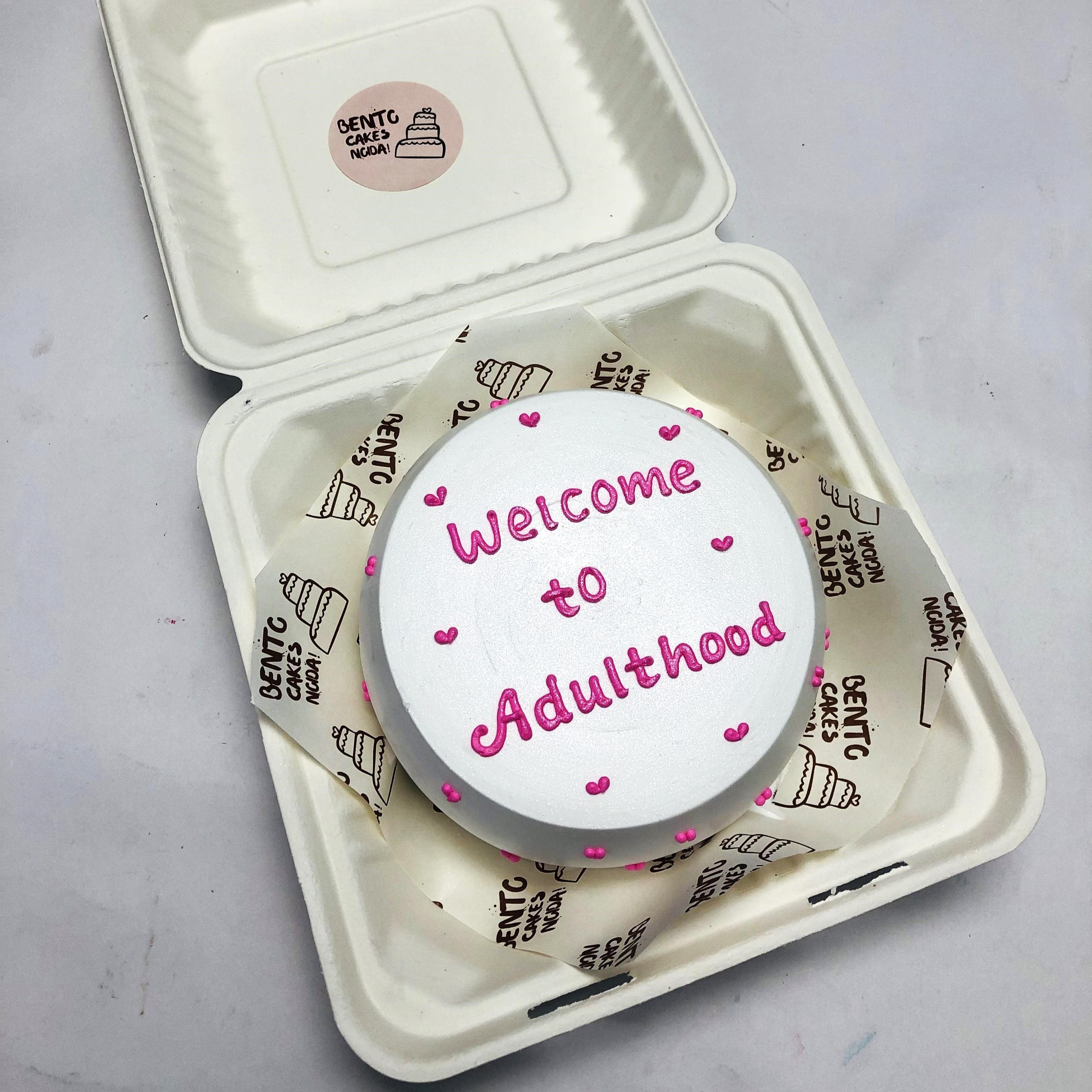 A pearl white bento cake with "Welcome to Adulthood" text with pink color.