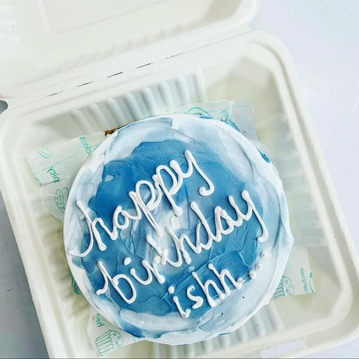 This Blue white frosting cake is designed for birthday and a text "happy birthday ishh" written with white icing on it.
