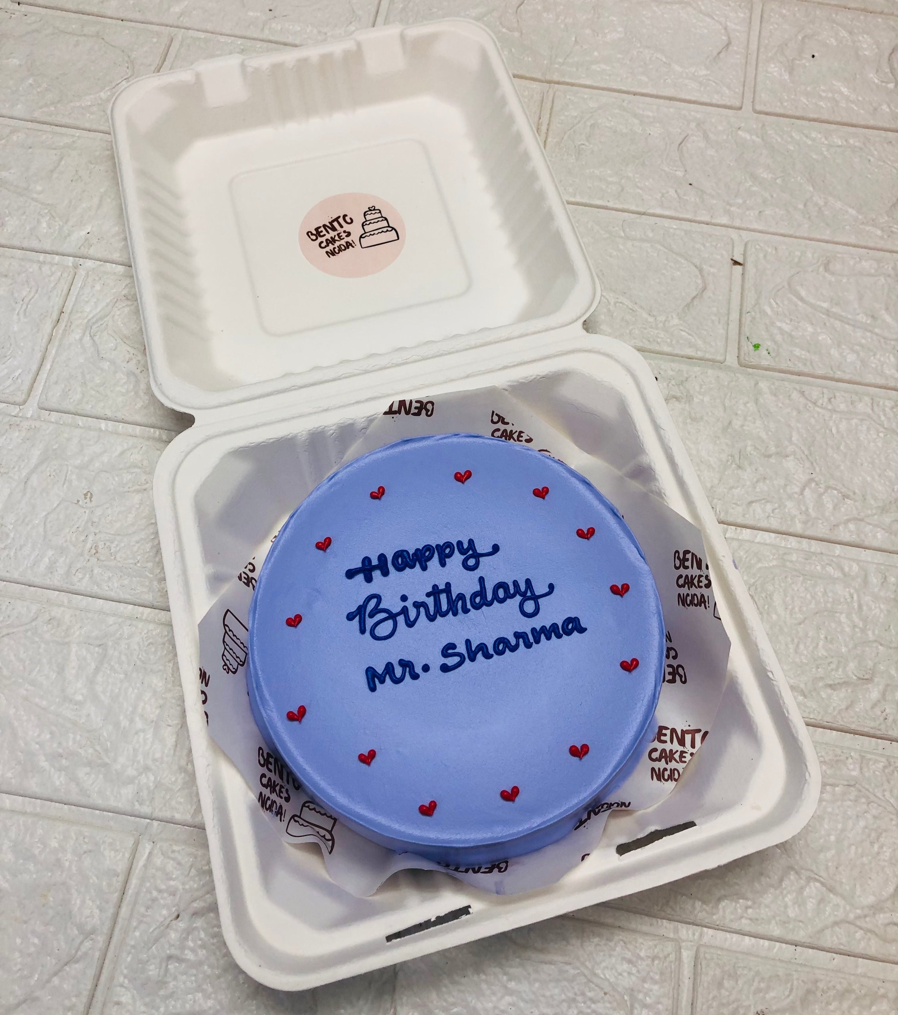 A blue bento cake is designed with little red heats on bounary with happy birthday text.