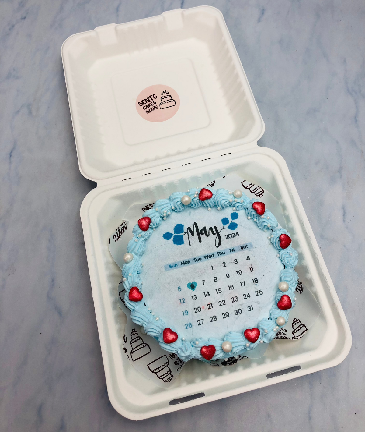 A light blue fire bento cake with red hearts and white sprinkles on its boundary.