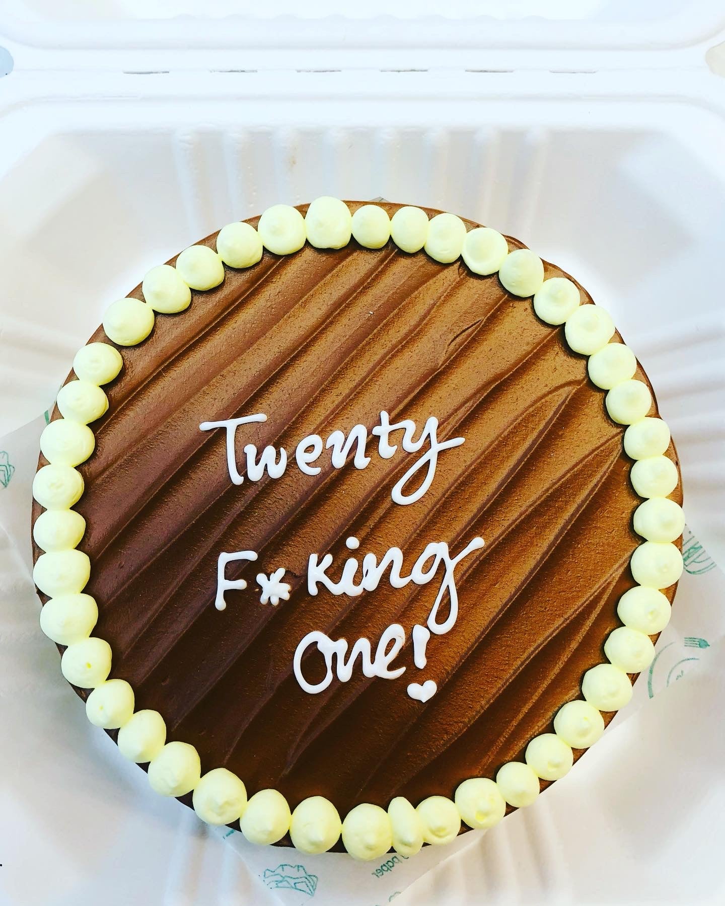 A chocolate cake with yellow icing border and white icing text that reads "Twenty F*king One!" inside a white container.