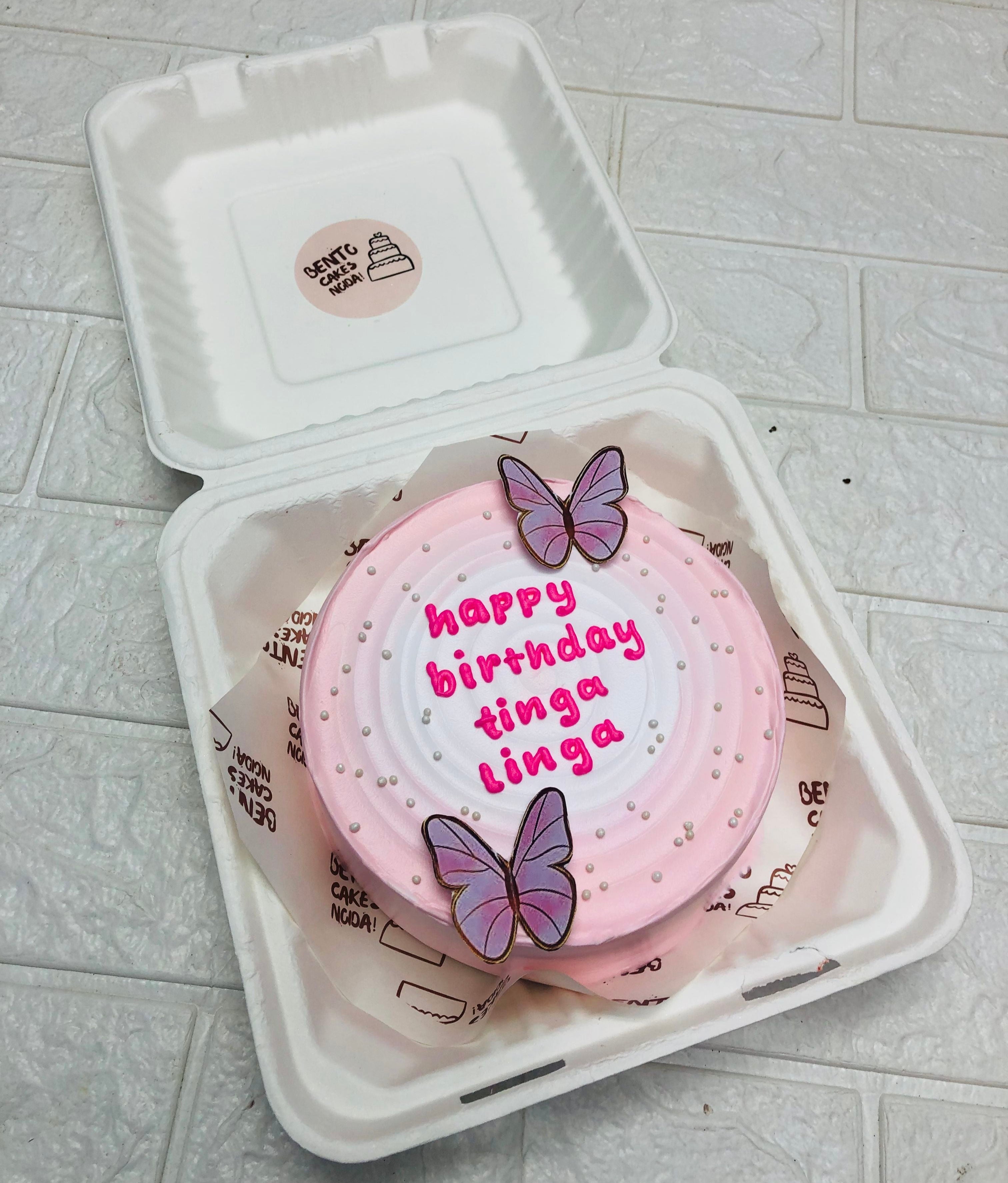 Aesthetic pink bento cake with white wavy shades, decorated with blue butterflies. 
