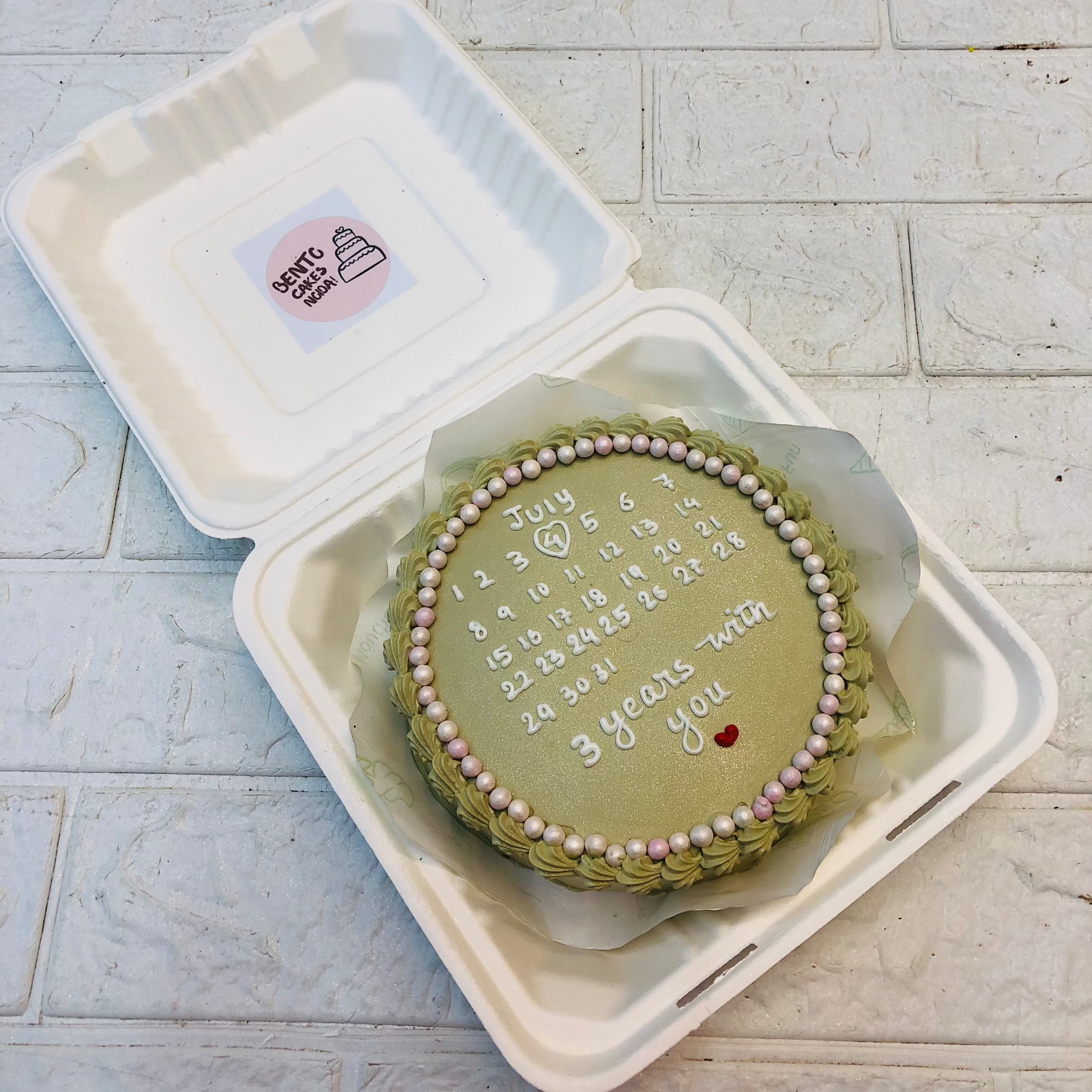 A shiney green bento cake having 3 years anniversary calendar design.