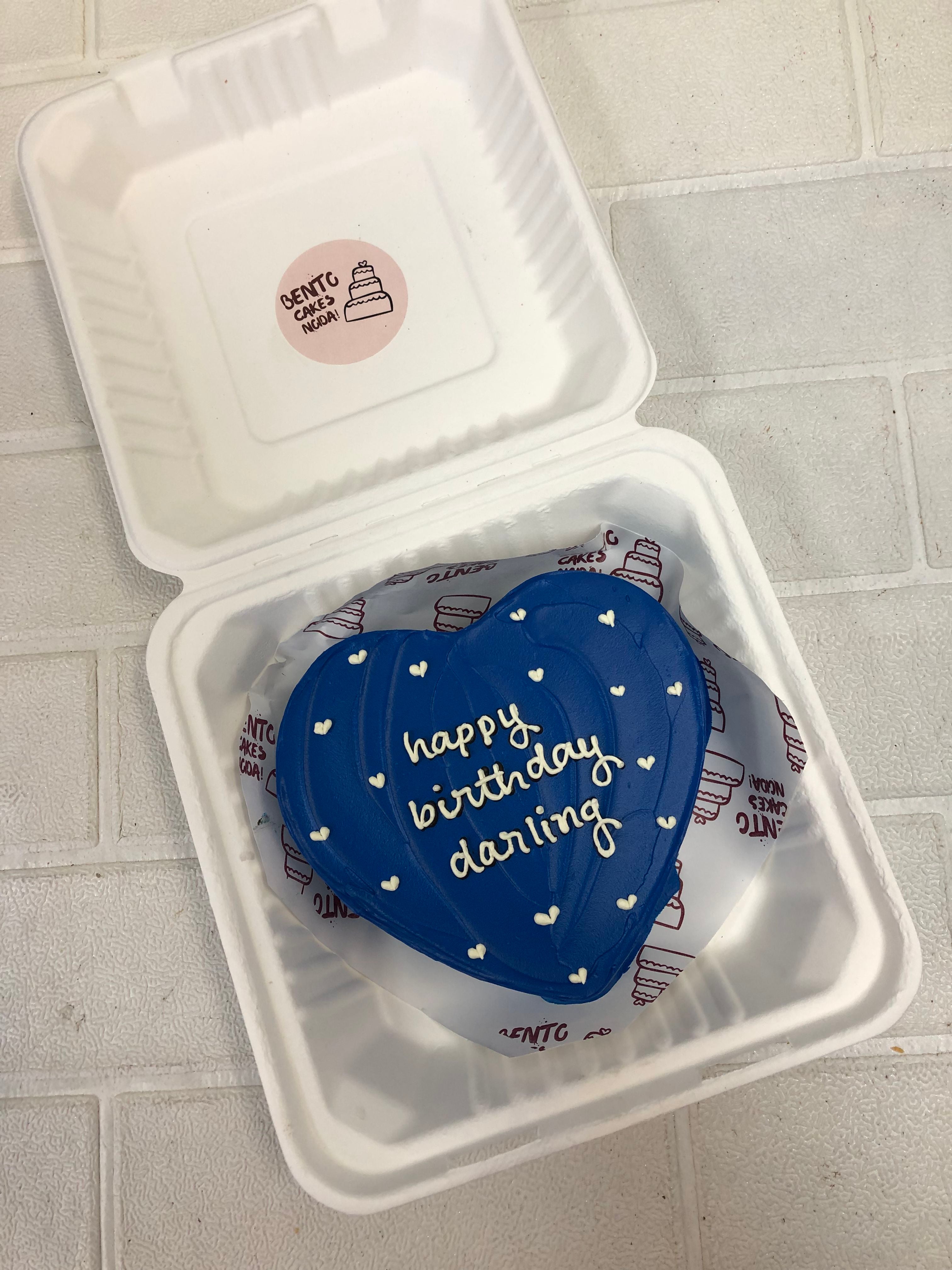 A aesthetic dark blue heart shape cake with pretty white hearts design and a loving text written on it hite icing on it.