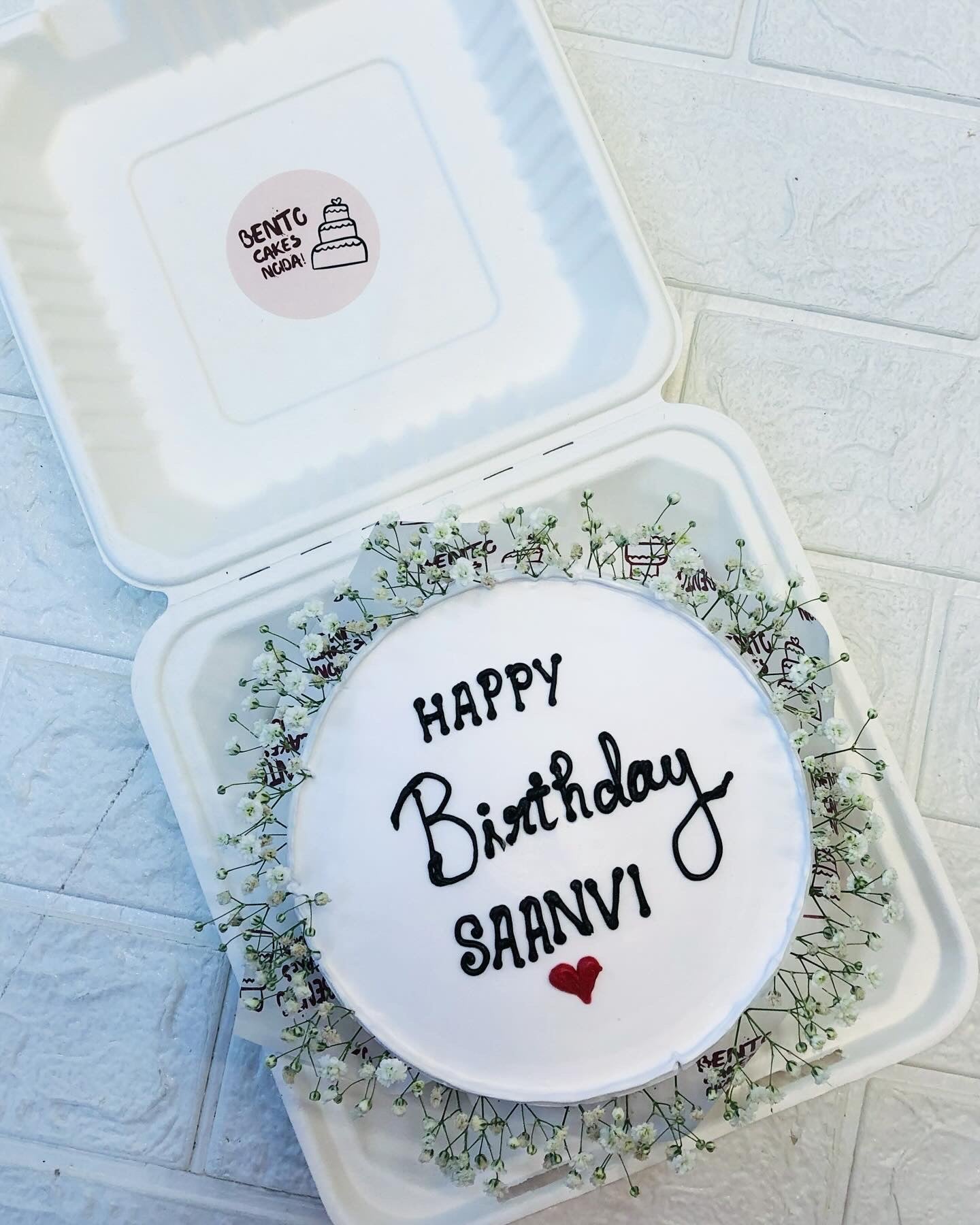 A white bento cake with blak birthday text and decorated with vintage florals.