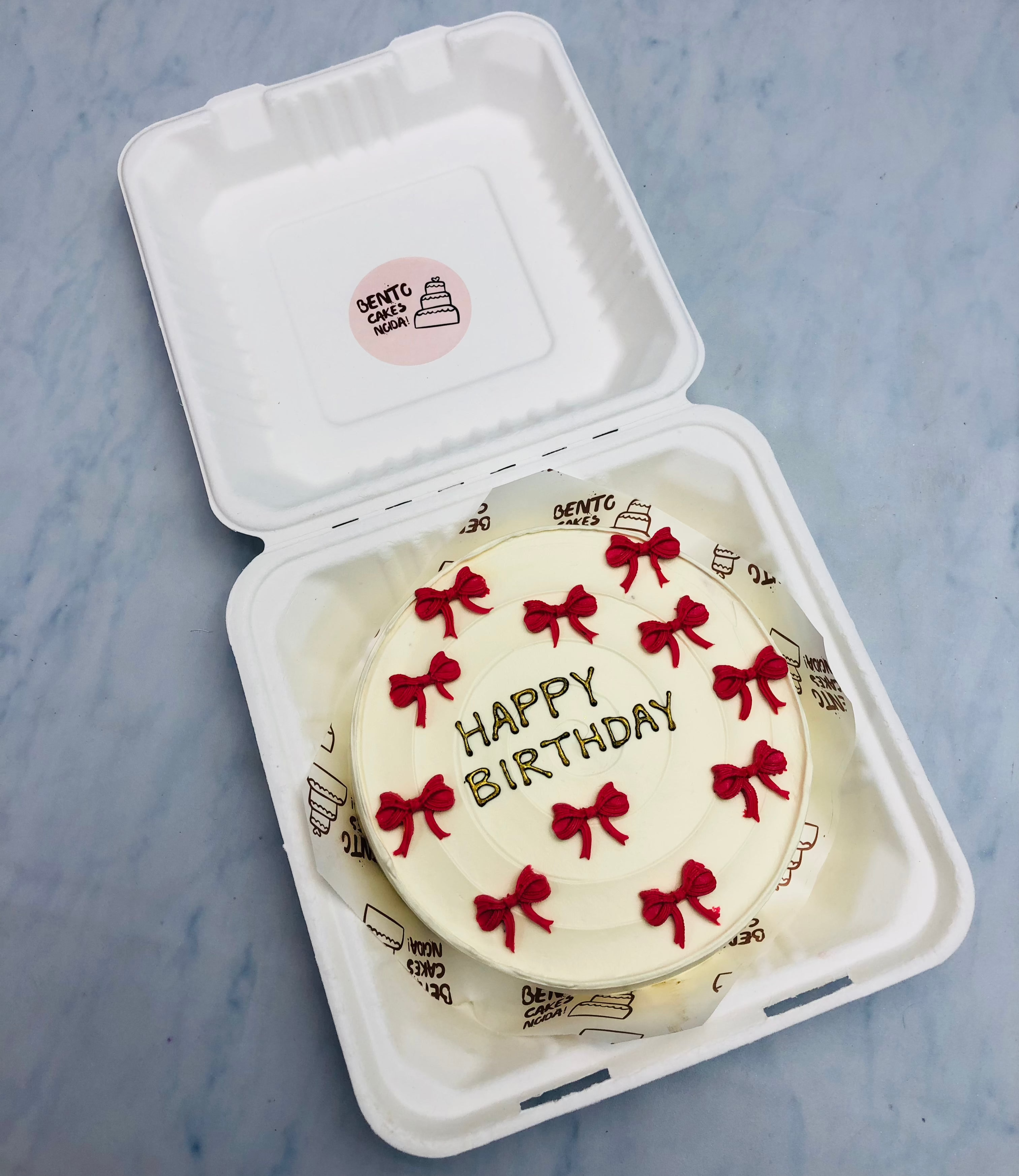A white bento cake designed with red bows design with cream for birthday.