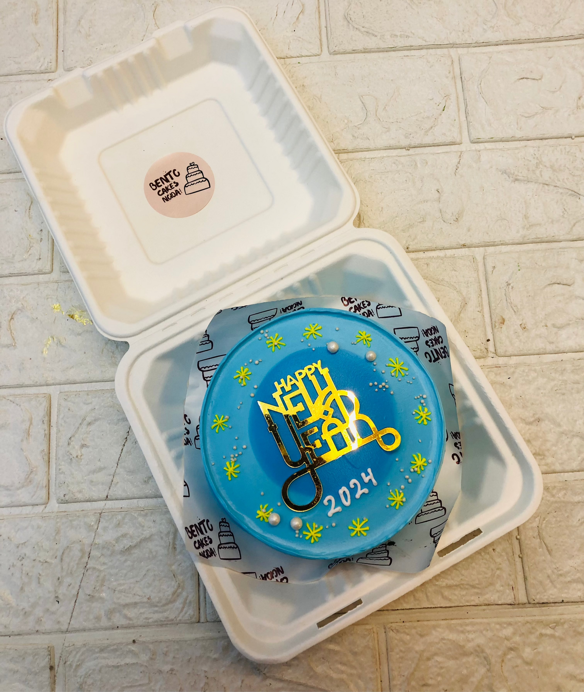 A skblue bento cake with a blue circular shade on the center with some yellow stars design for celebrating new year.