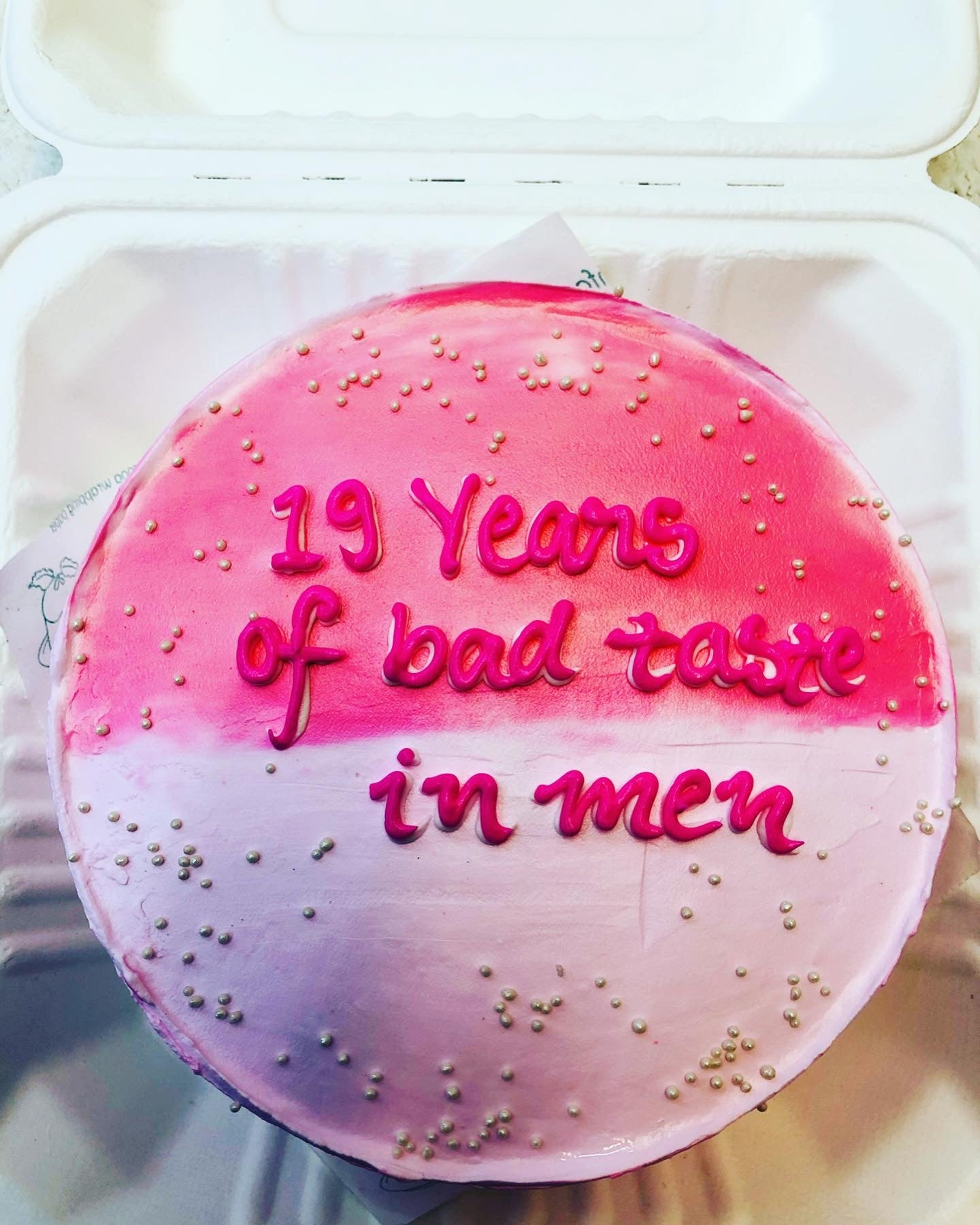A pink icing cake is decorated with white sprinkles on it and a text "19 Years of bad taste in men" written with pink color on it.
