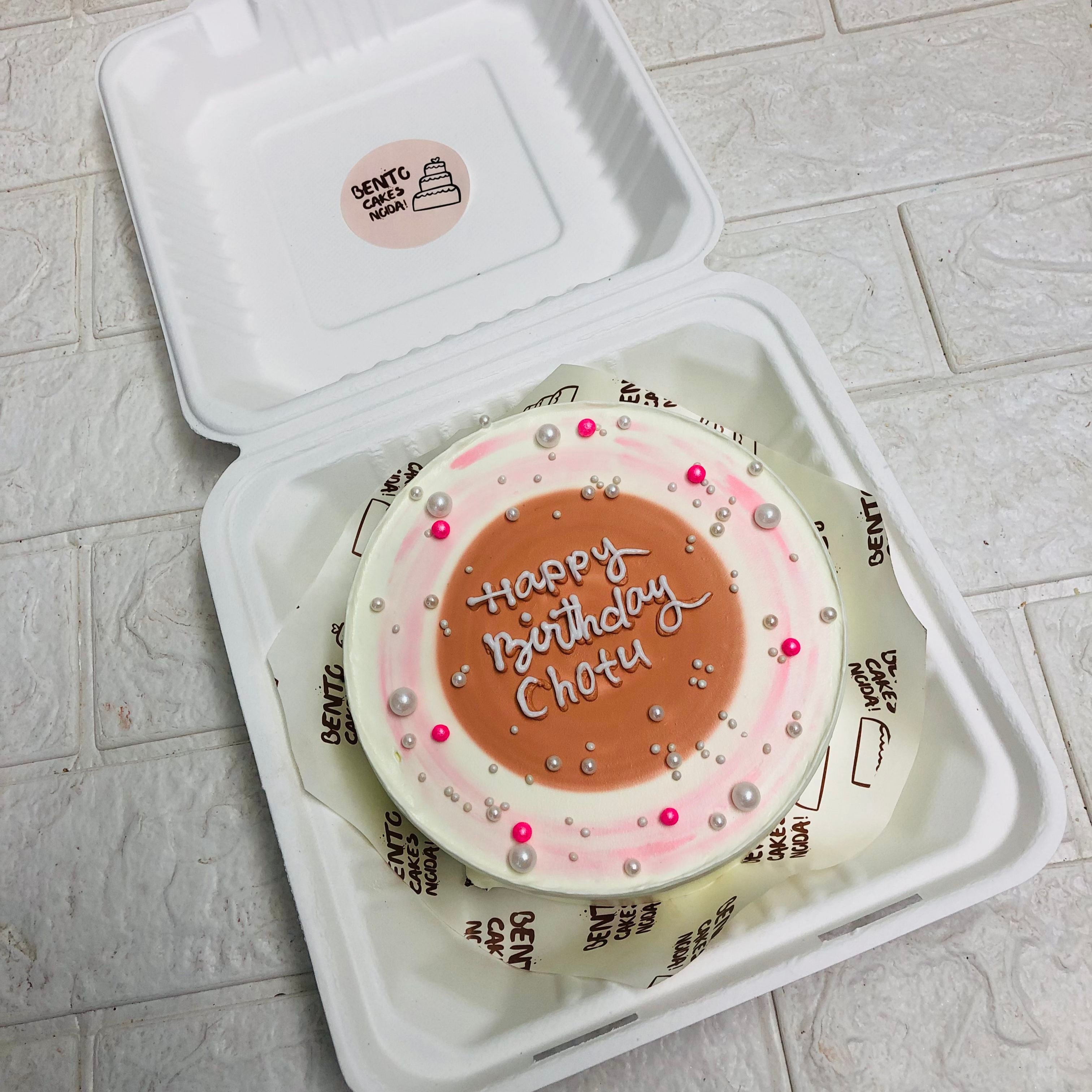 A white box showcasing a beautifully decorated pink and white cake, perfect for birthday celebrations.