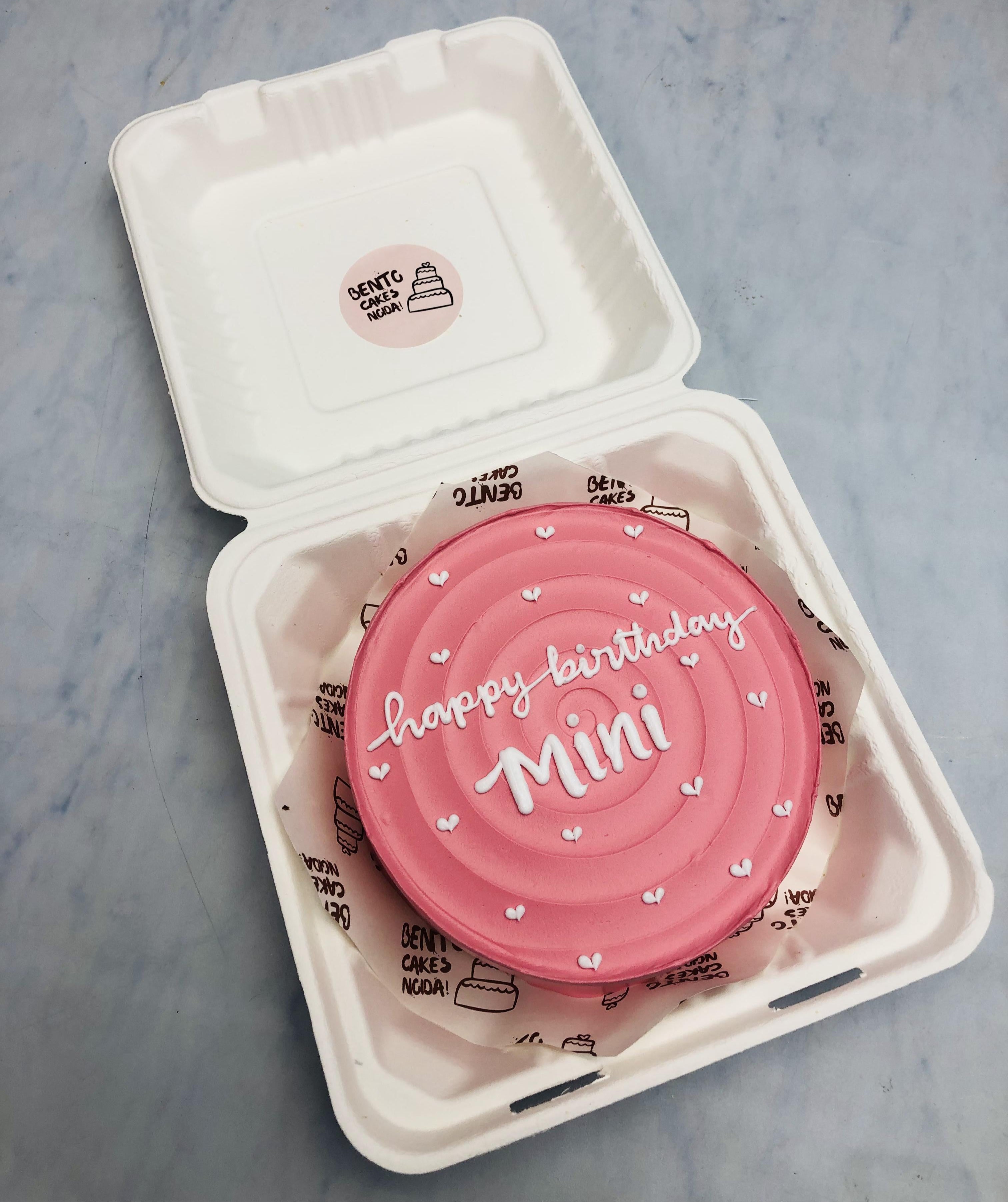 Awsthetic pink birthday bento cake decorated with pretty white hearts and a text "happy birthday Mini" written with white icing.