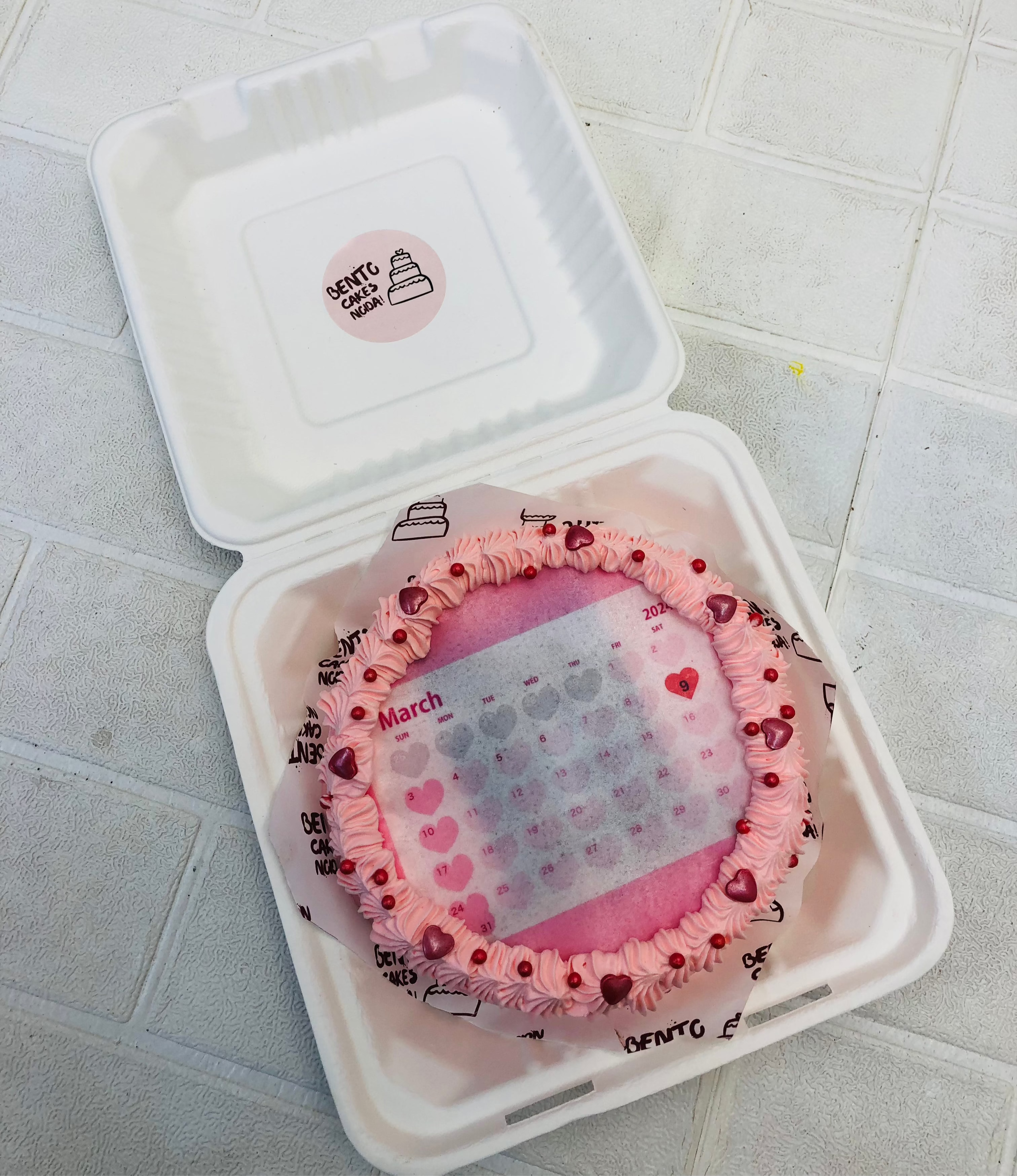 An aesthetic pink fire bento cake having hearts design on calendar.
