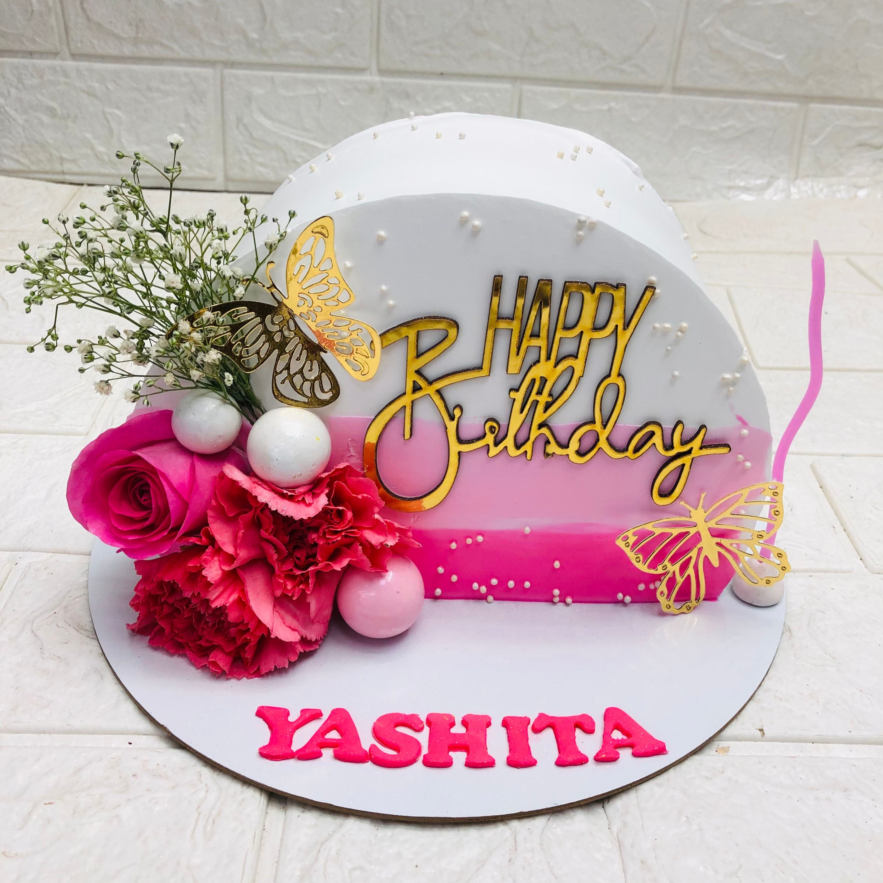 A decorated cake displaying a birthday tag, and flowers added in Half shape design. 