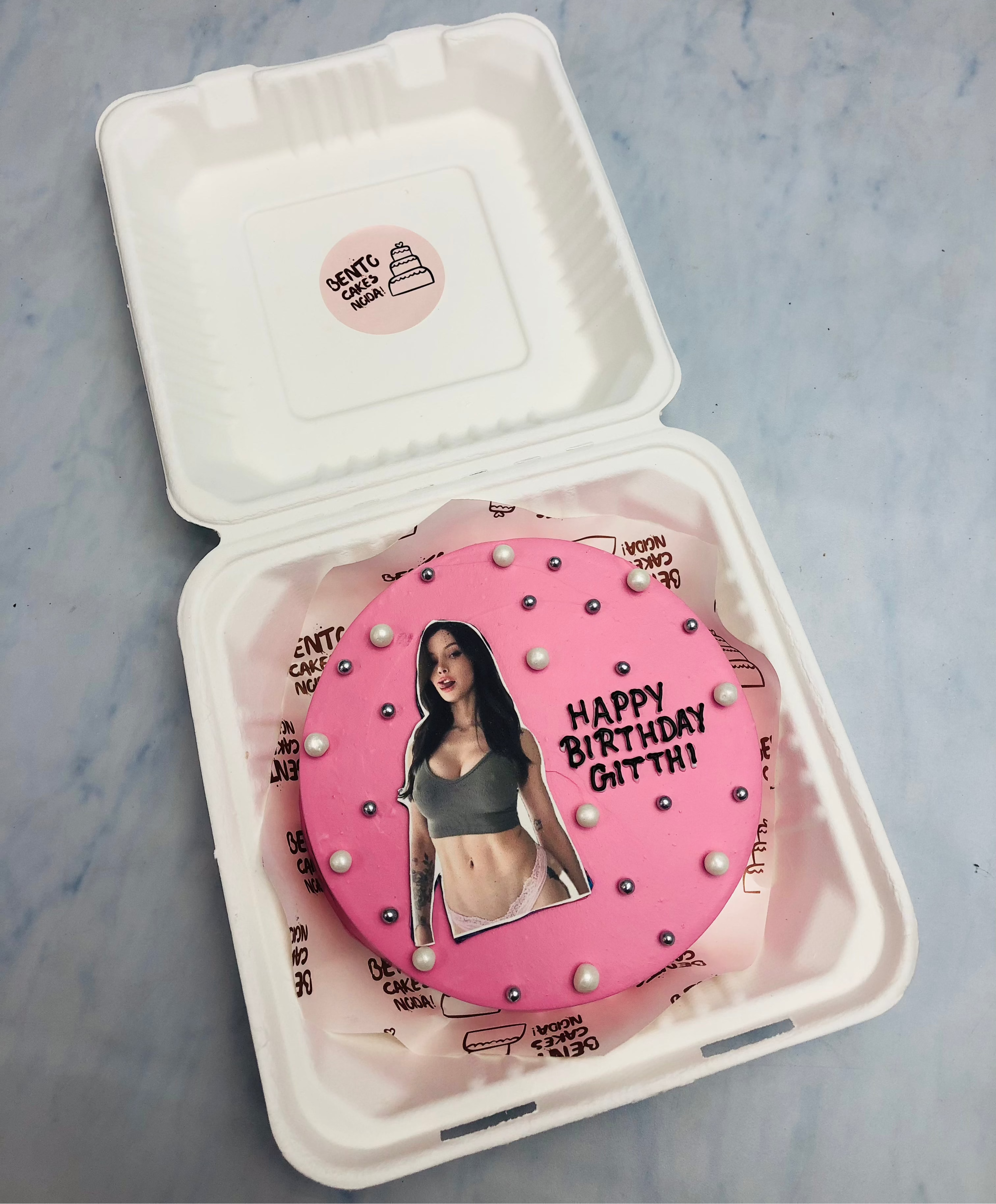 A pink bento cake designed for bitrthday of a girl having her image in bikney and cake decorated with white and silver sprinkles.