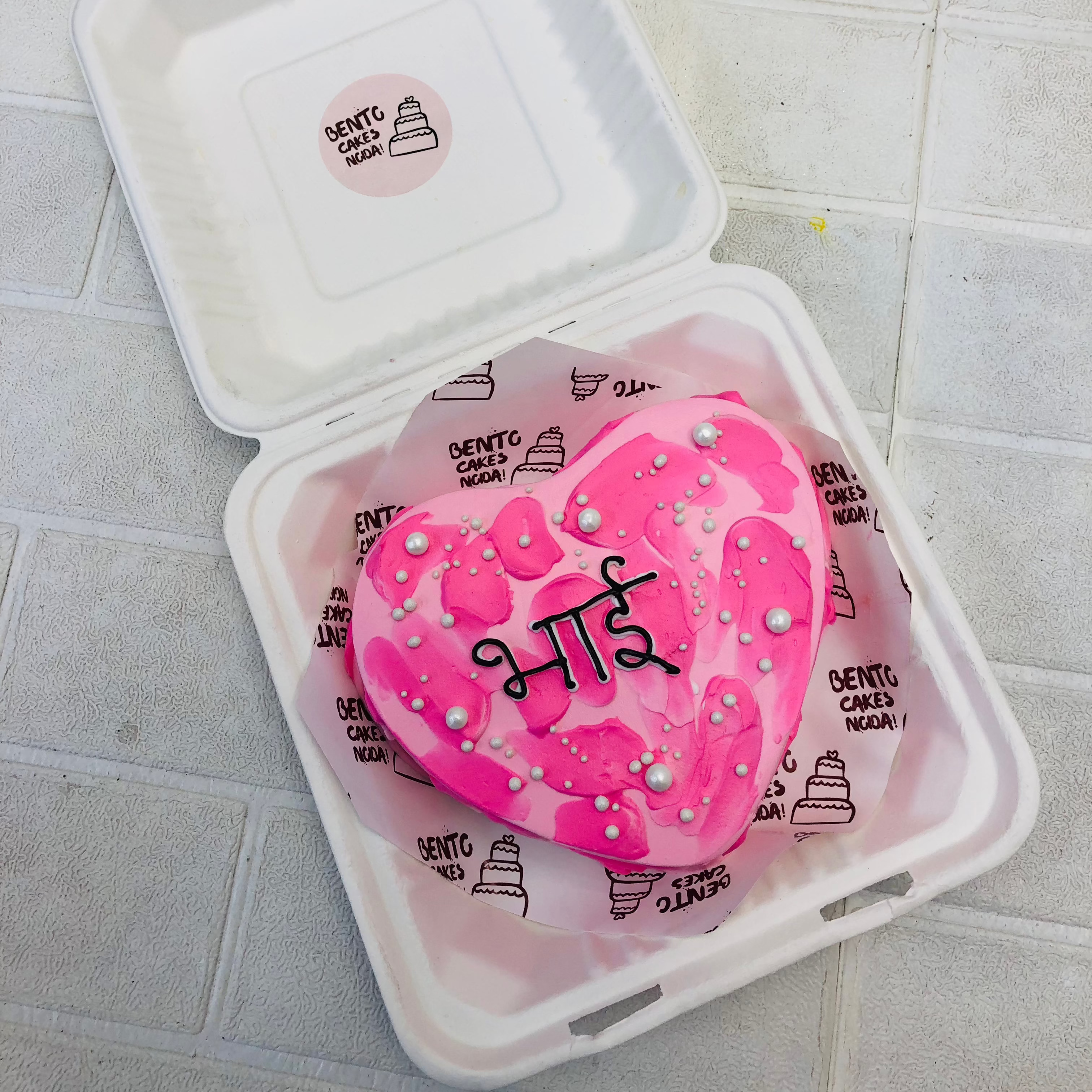 A pink heart shape cake with dark pink shades on it and a "Bhai" tect reitten in hindi.