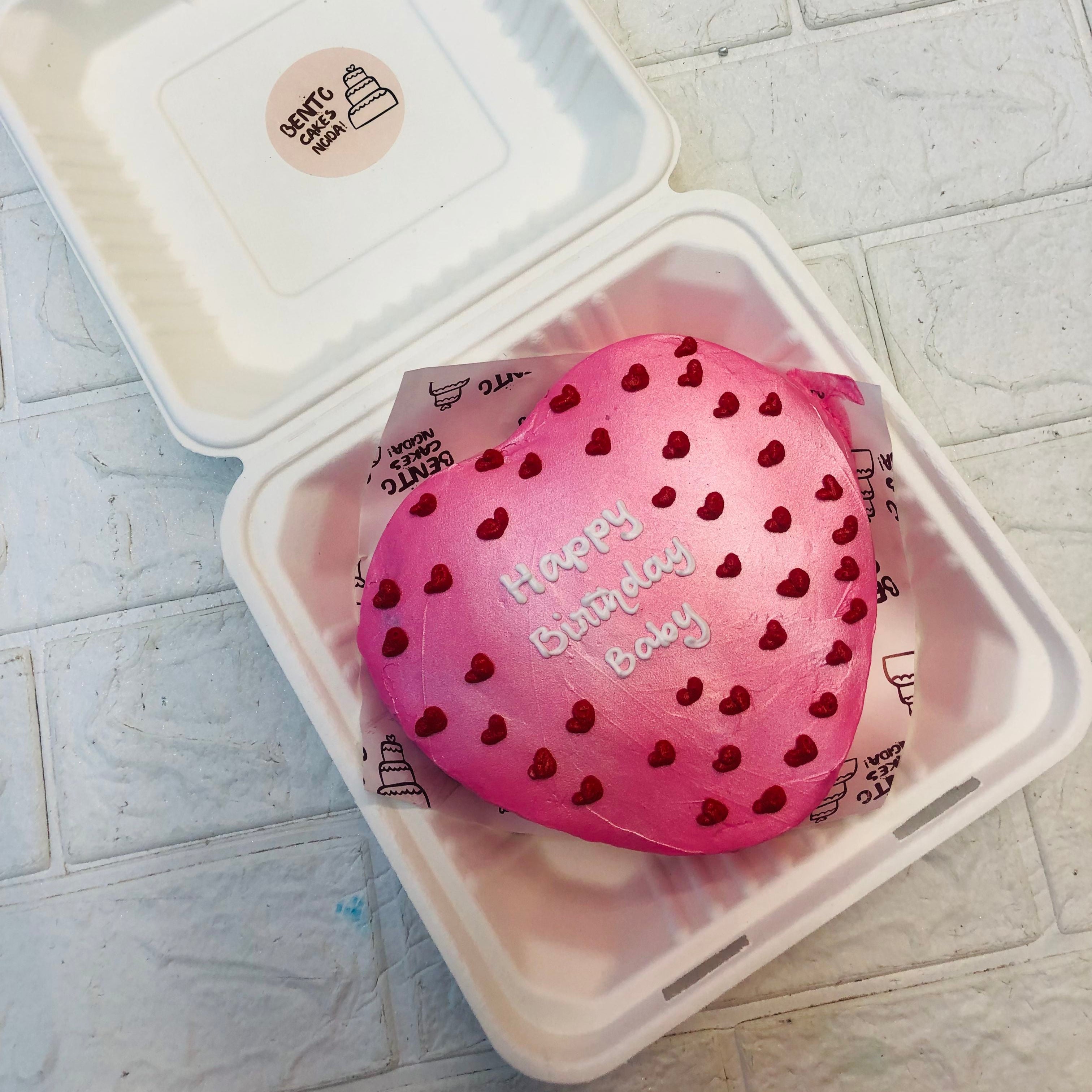 An Aesthetic Pink color Heart Shape Bento Cake with pretty red hearts design on it and a "Happy Birthday Baby" written on it.