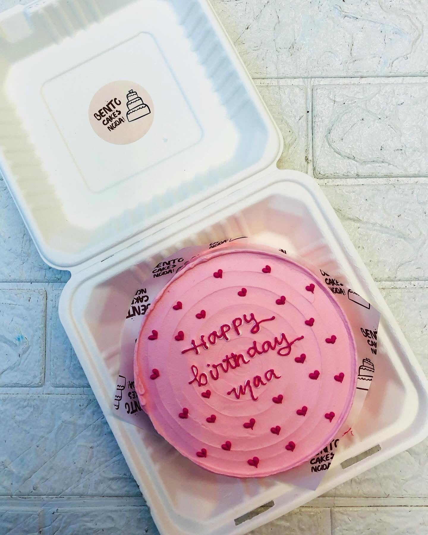 A pink cake with circular design on top and decorated with little pink hearts for moms birthday.