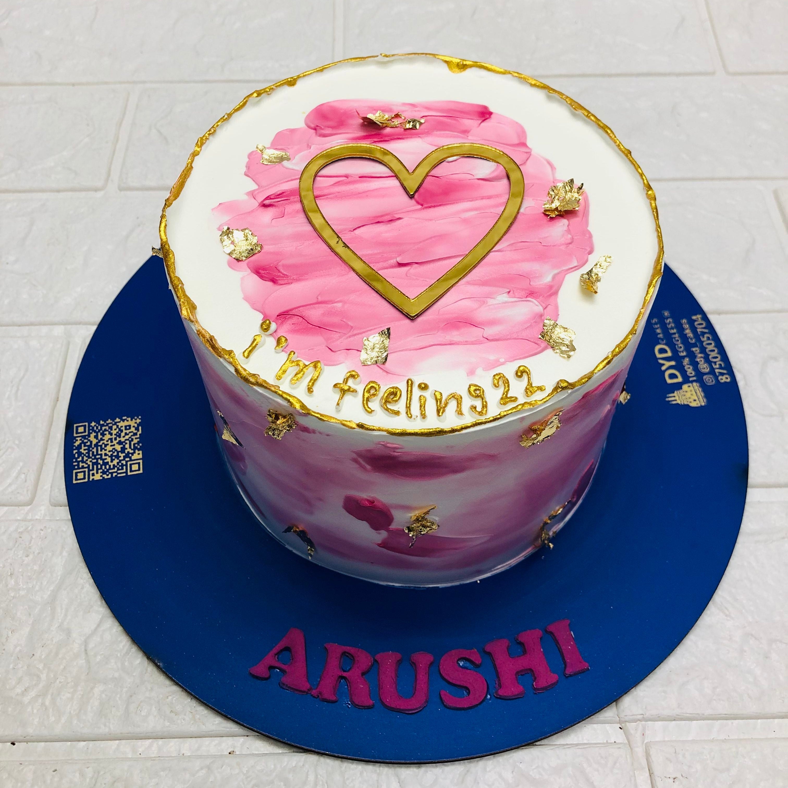 A white cake with pink icing on top and its sides, decorated with golden work designed for girls birthday celebration.