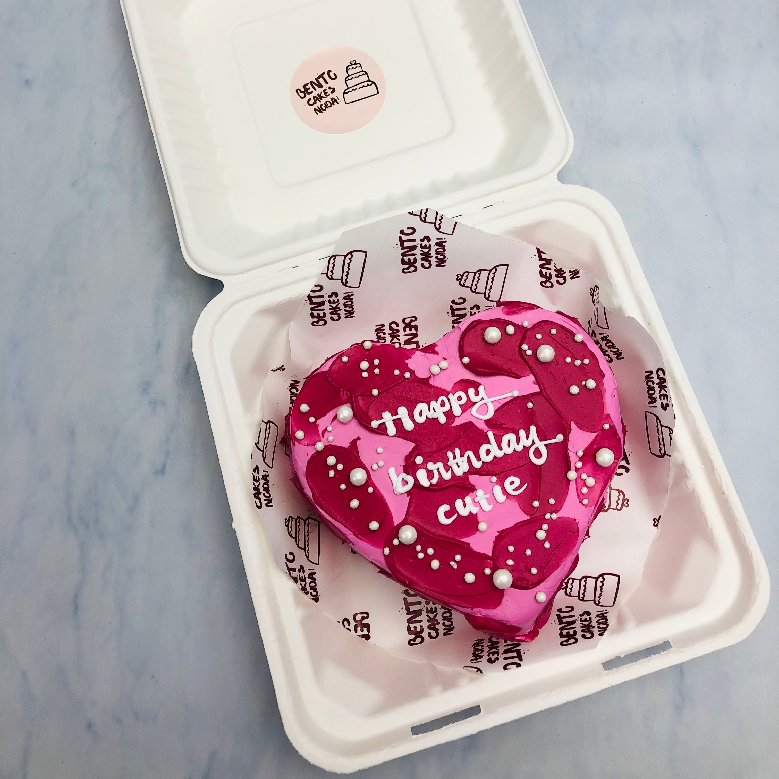 A pink heart shape cake with dark pink shades on it and decorated with white sprinkles.