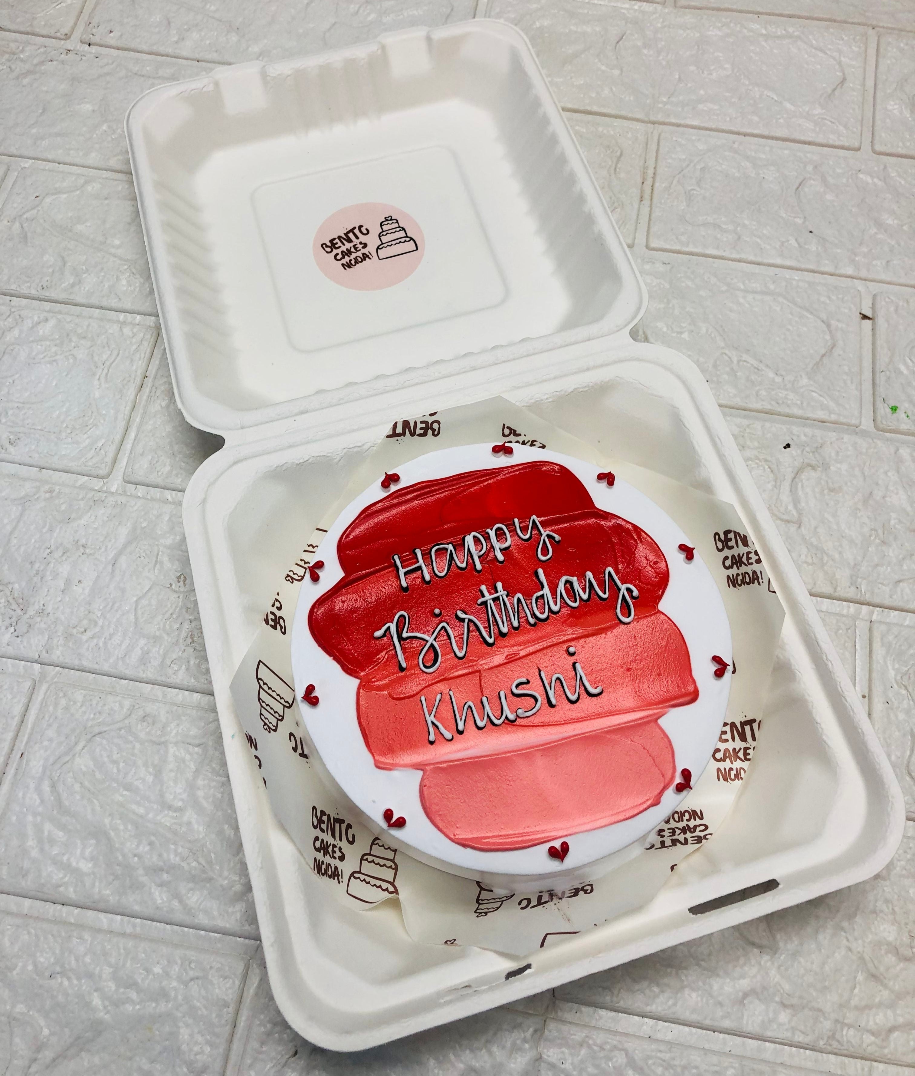 A white bento cake with red shades and surrounded with little red heats.