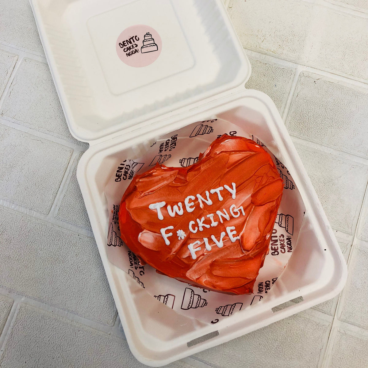 A dark red heart shape cake with red white shades on it and a text written with white icing on it.