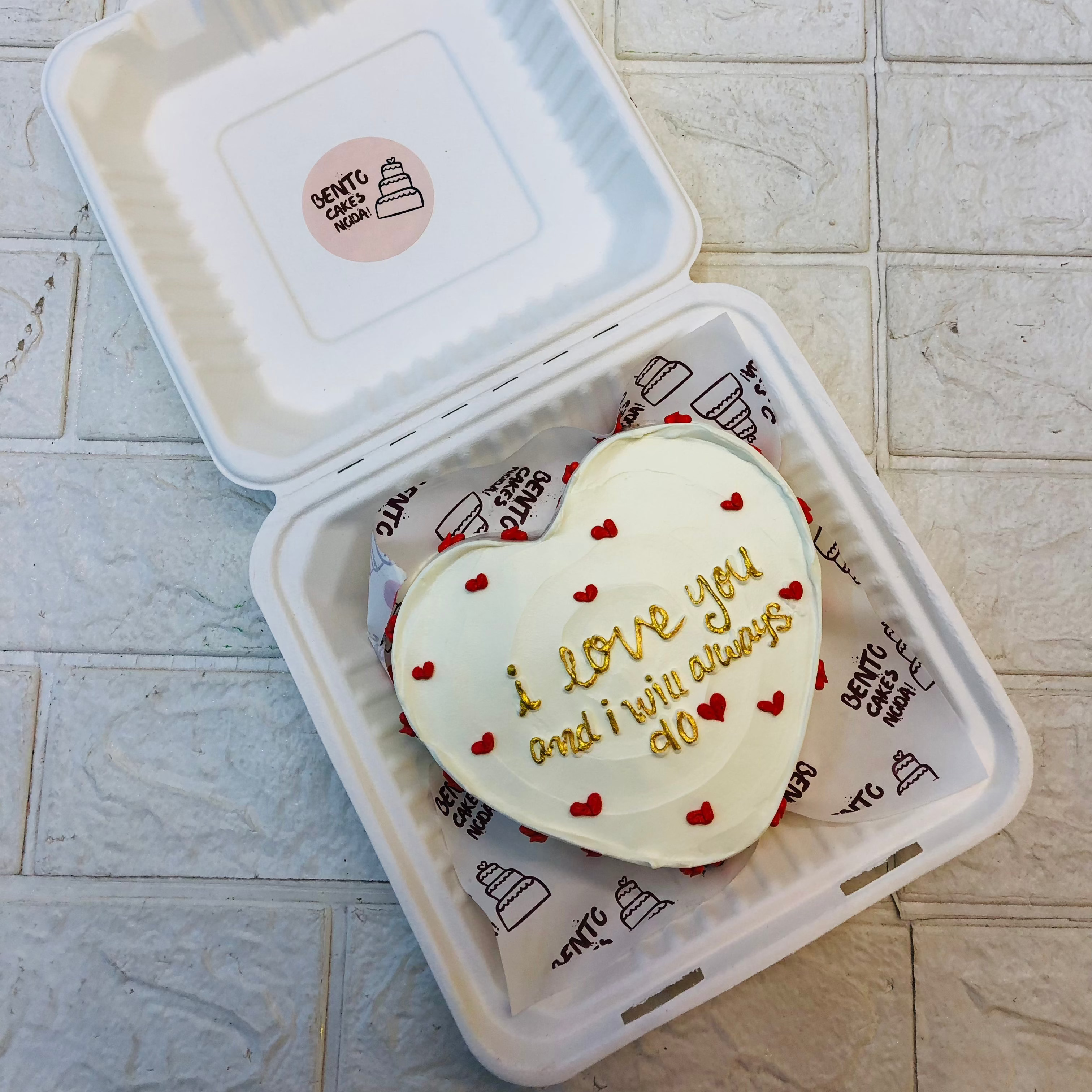 An ffwhite heart shape cake filled with red hearts all over the cake and a loving text written with golden color.