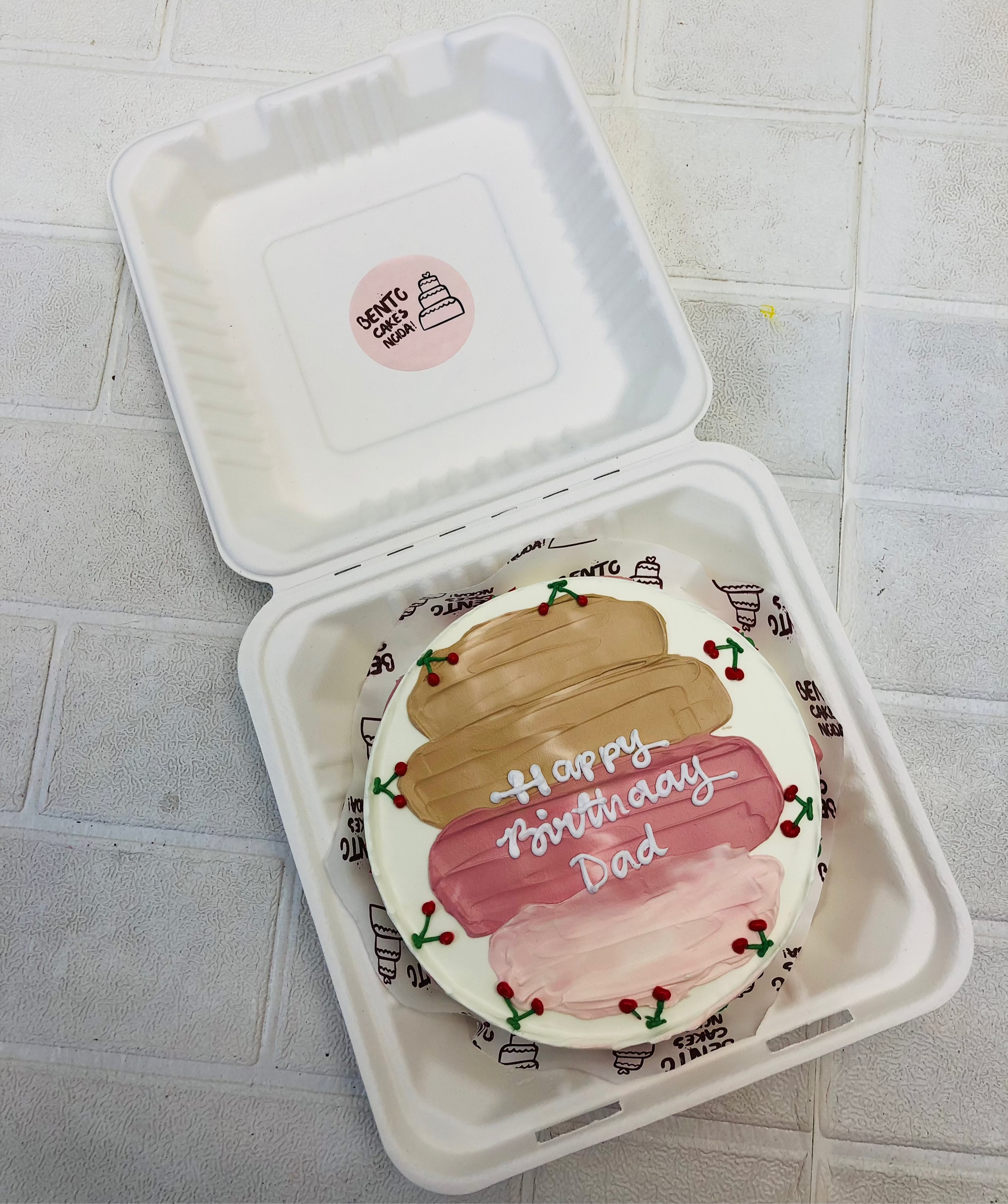 A white bento cake having brown pink shades on cake with some cherry designs.