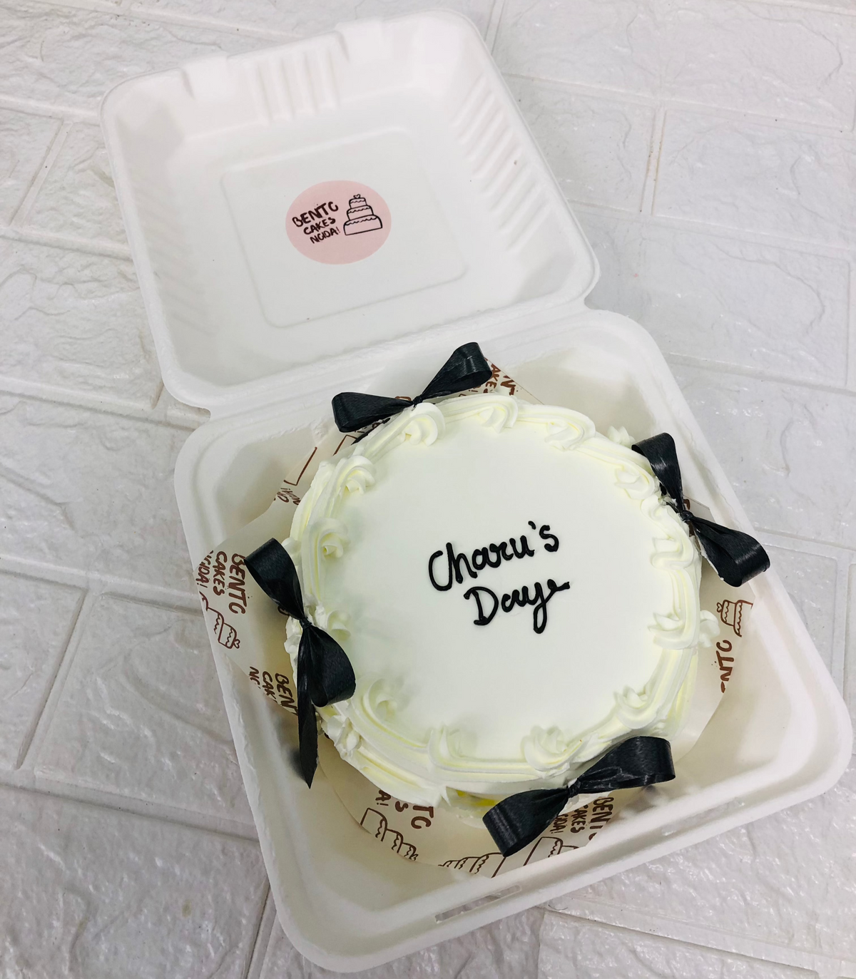 A white vintage bento cake decorated with black bows for birthday.