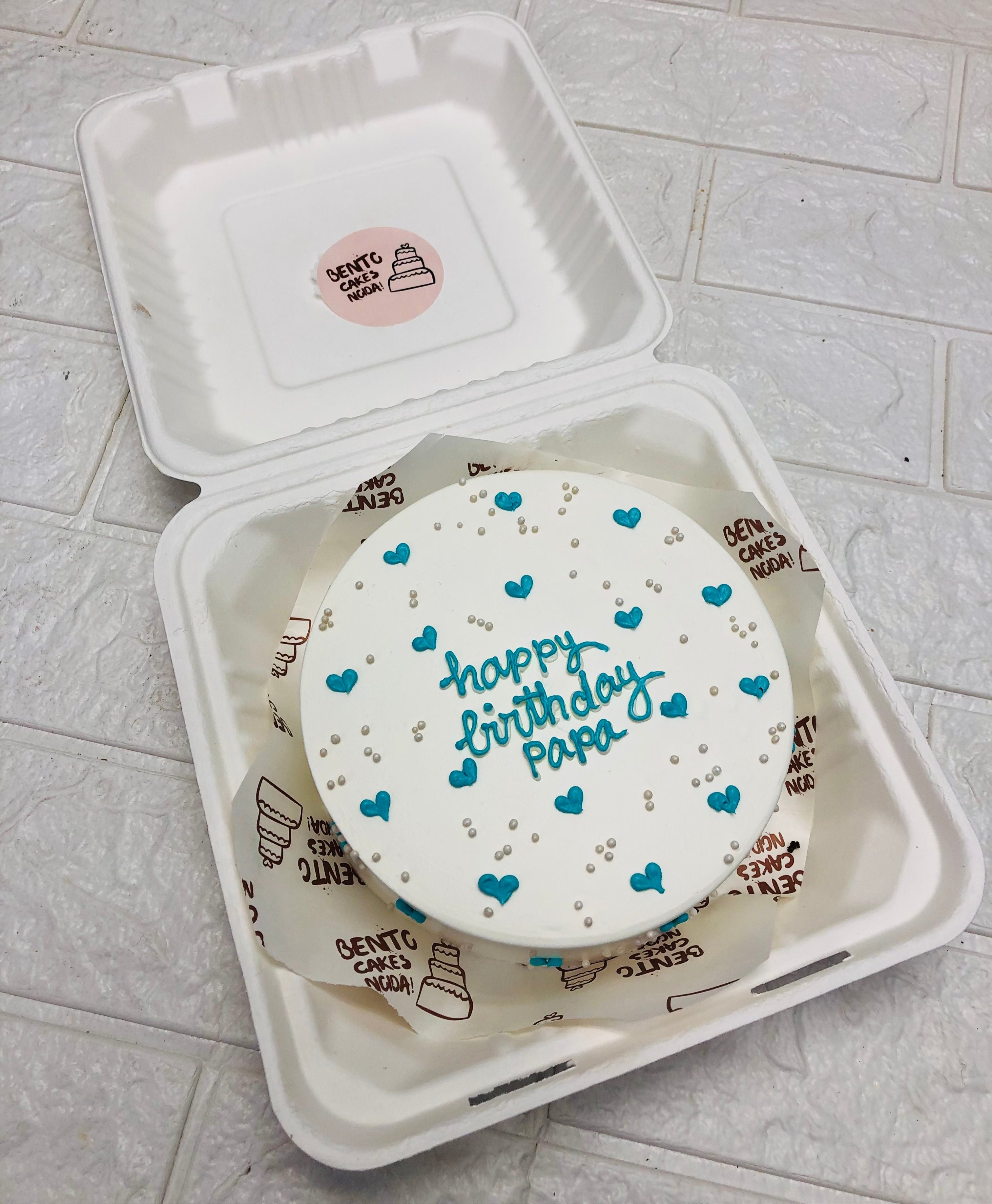 Aesthetic white birthday bento cake is designed for fathers birthday and deorated with blue hearts and sprinkls.