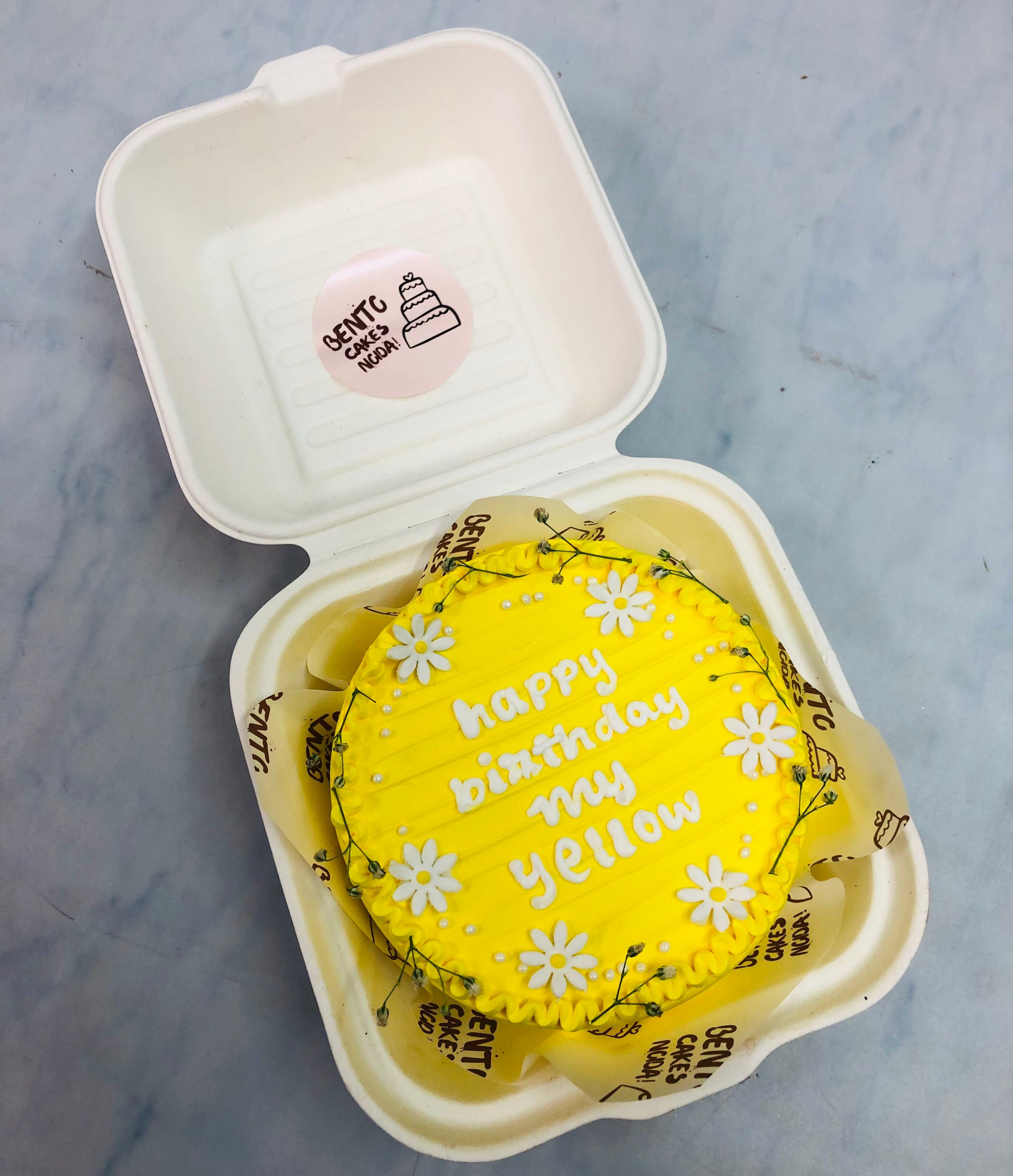 A yellow icing bento cake decorated with white florals and a text "happy birthday my yellow" written with white icing.