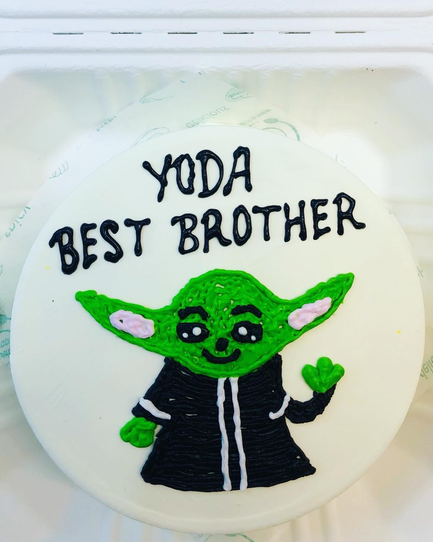 A white cake in a bento box, designed with a alien design on its top and a text "YODA BEST BROTHER" written on it.