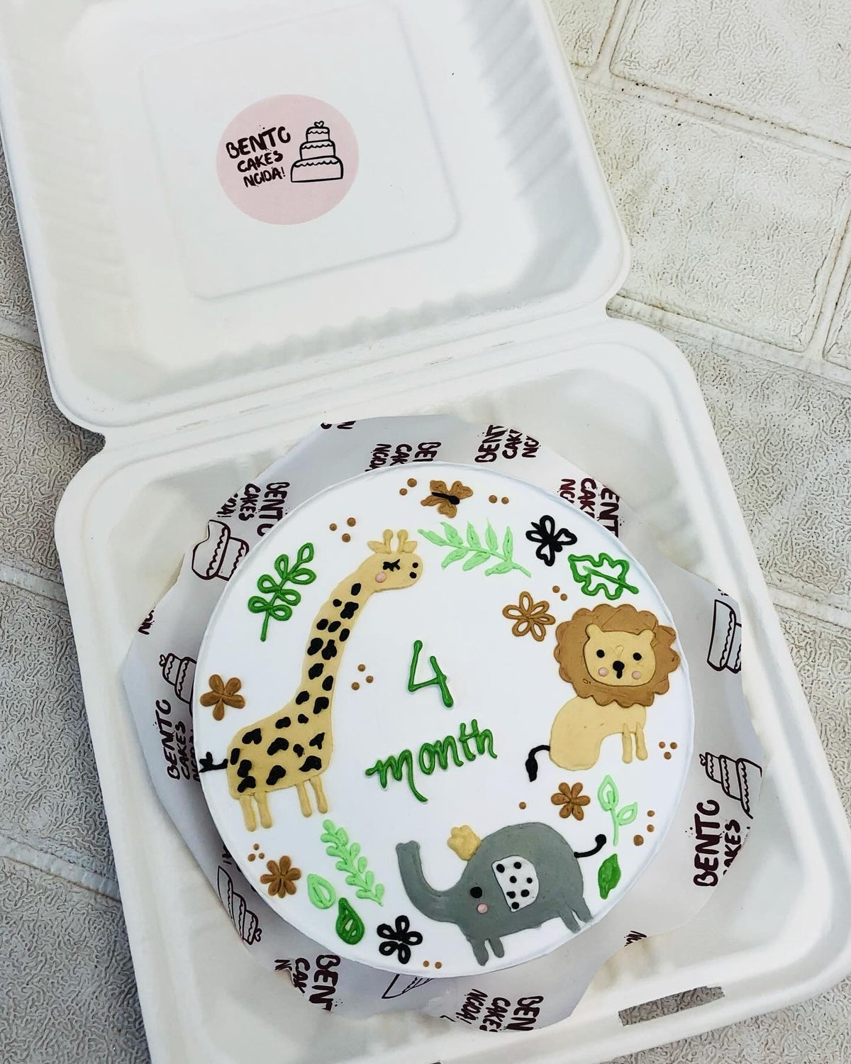 A white cake in a bento box designed with Girrafe, Lion and Elephant characters and gving a jungle look.
