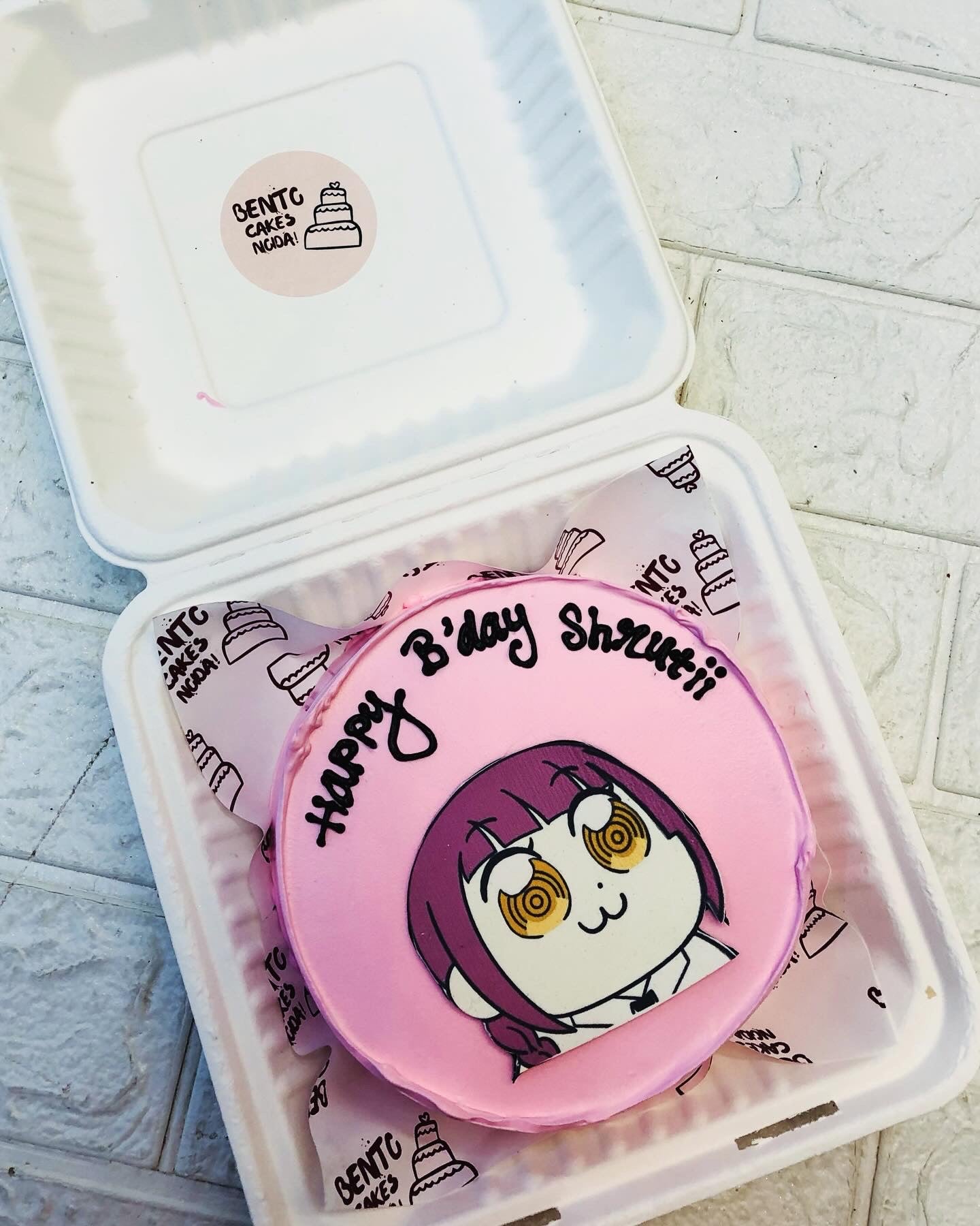 A pink birthday cake featuring an anime character design with purple hair and yellow spiral eyes, inscribed with "Happy B'day Shruthii".