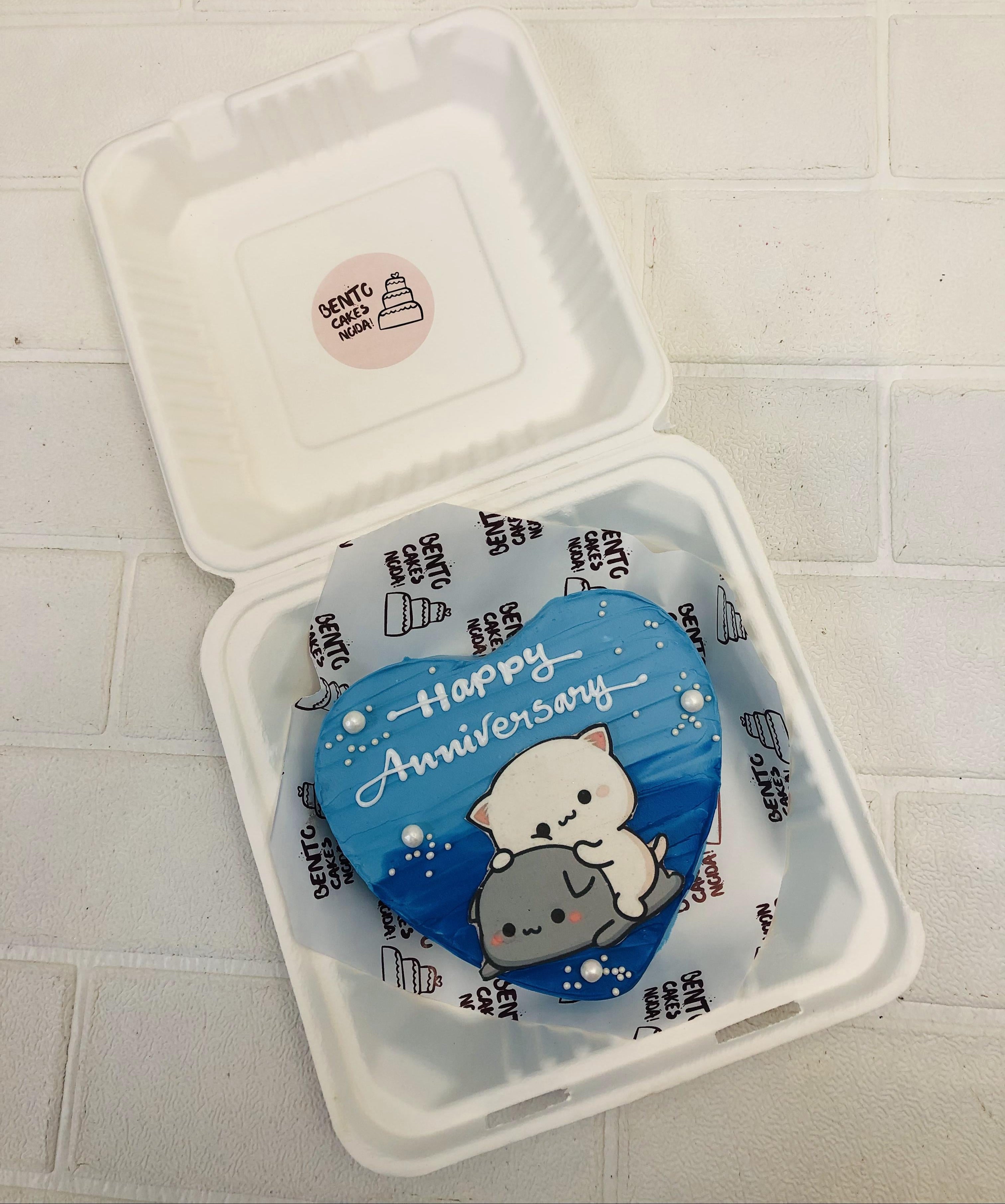 An aesthetic blue heart shape bento cake with dudu sitting on bubu print for anniversary occasion.