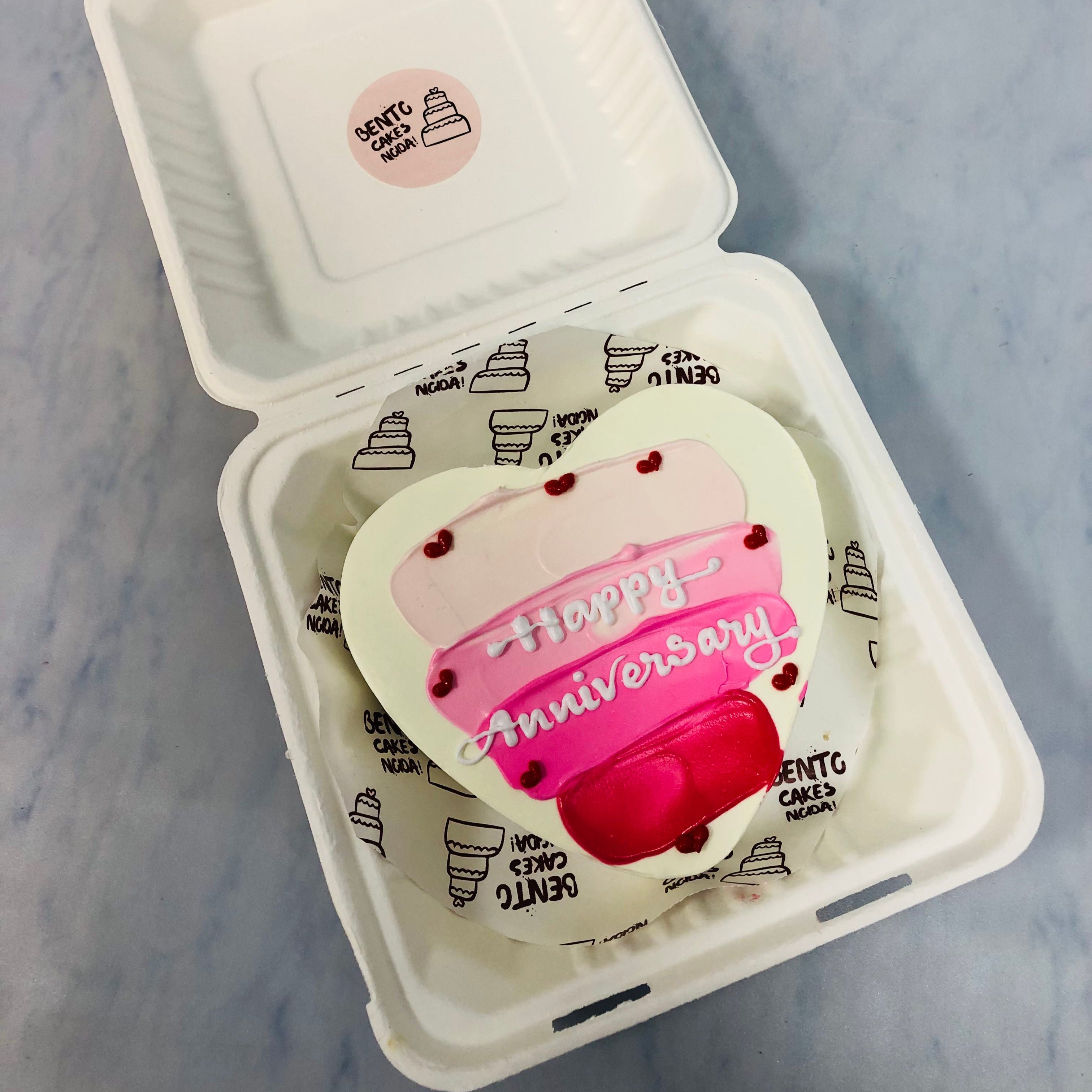 A white heart shape cake with 3 shades of pink color on it, is designed for anniversary.