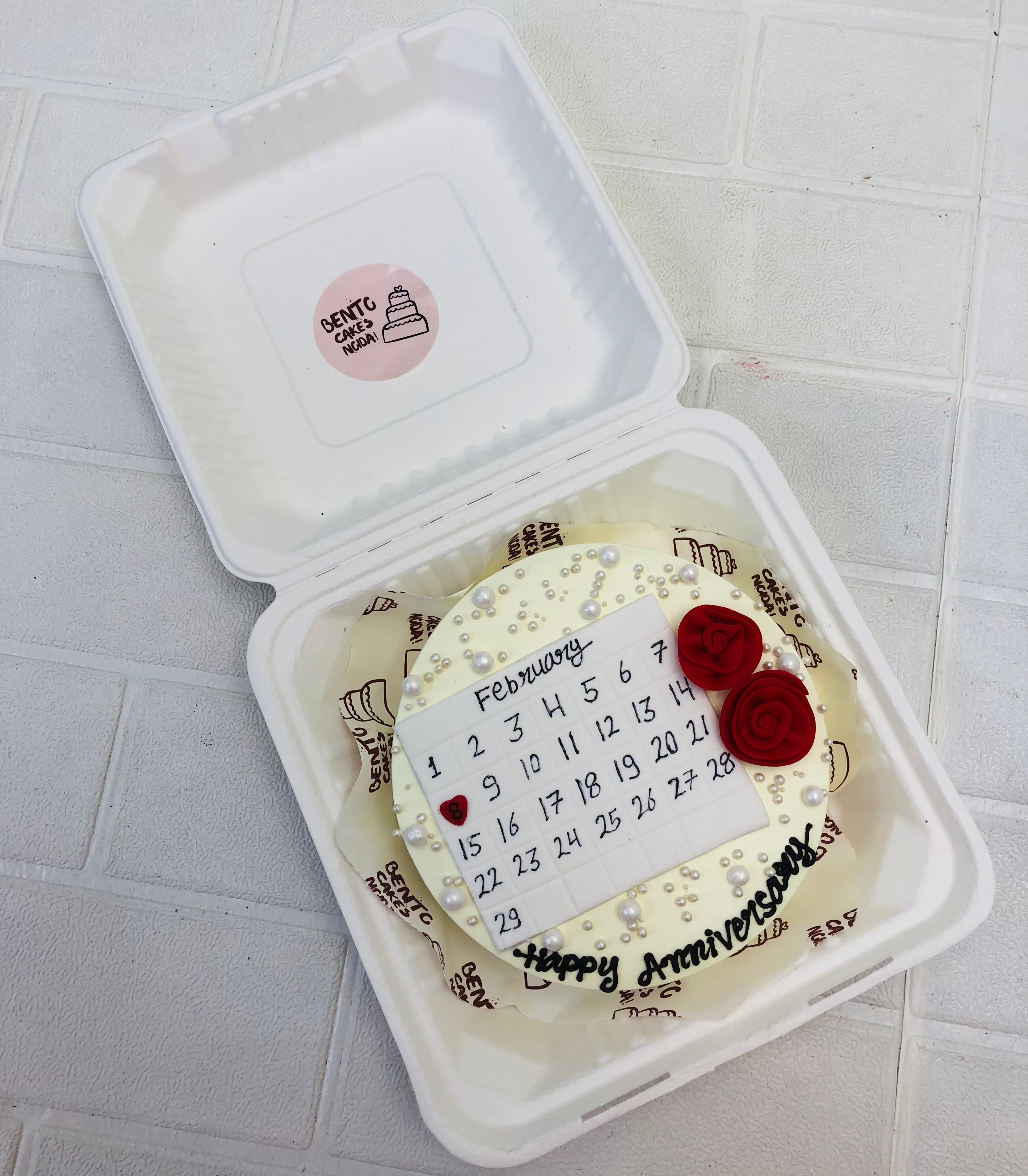 An off white bento cake habving fondant calendar design with red fondant roses.
