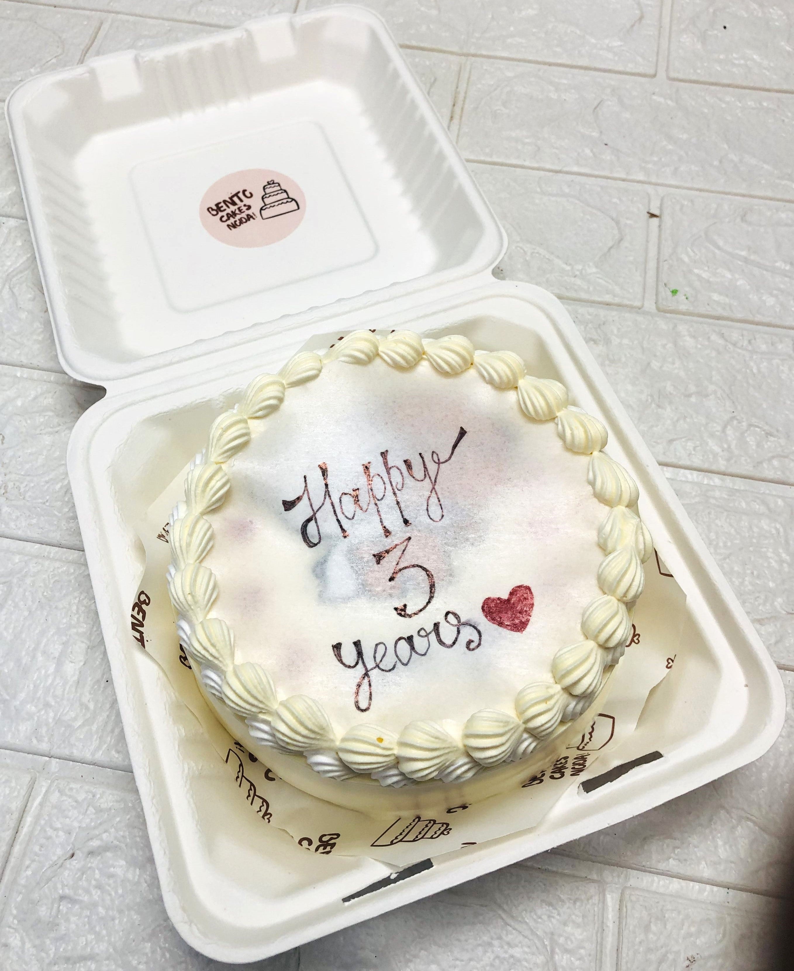A white bento cake having Happy 3 Years on fire paper for anniversary celebration.