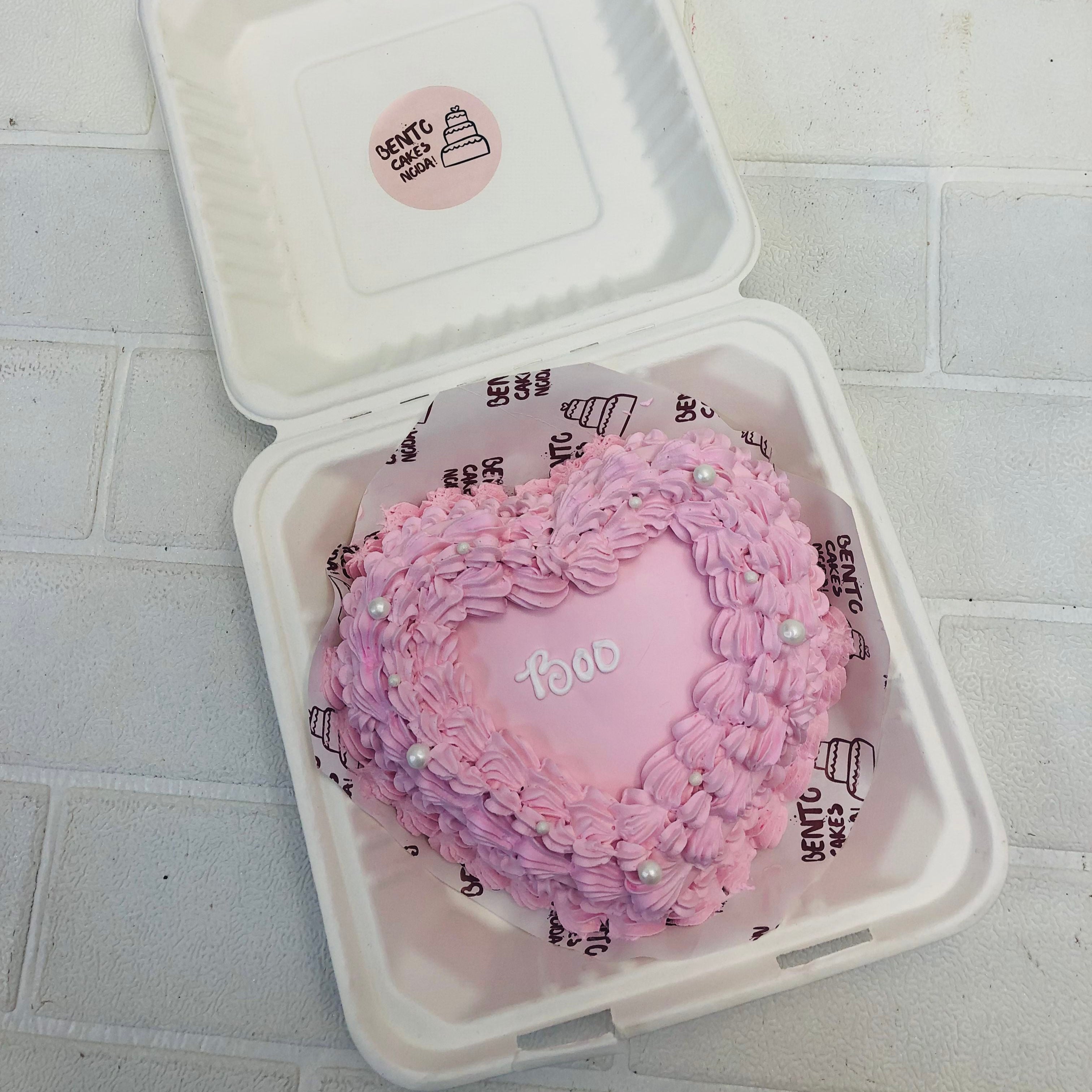 Am Attractive Heart Shape cake in a Bento box with pink floral design all around it with a "Boo" text.