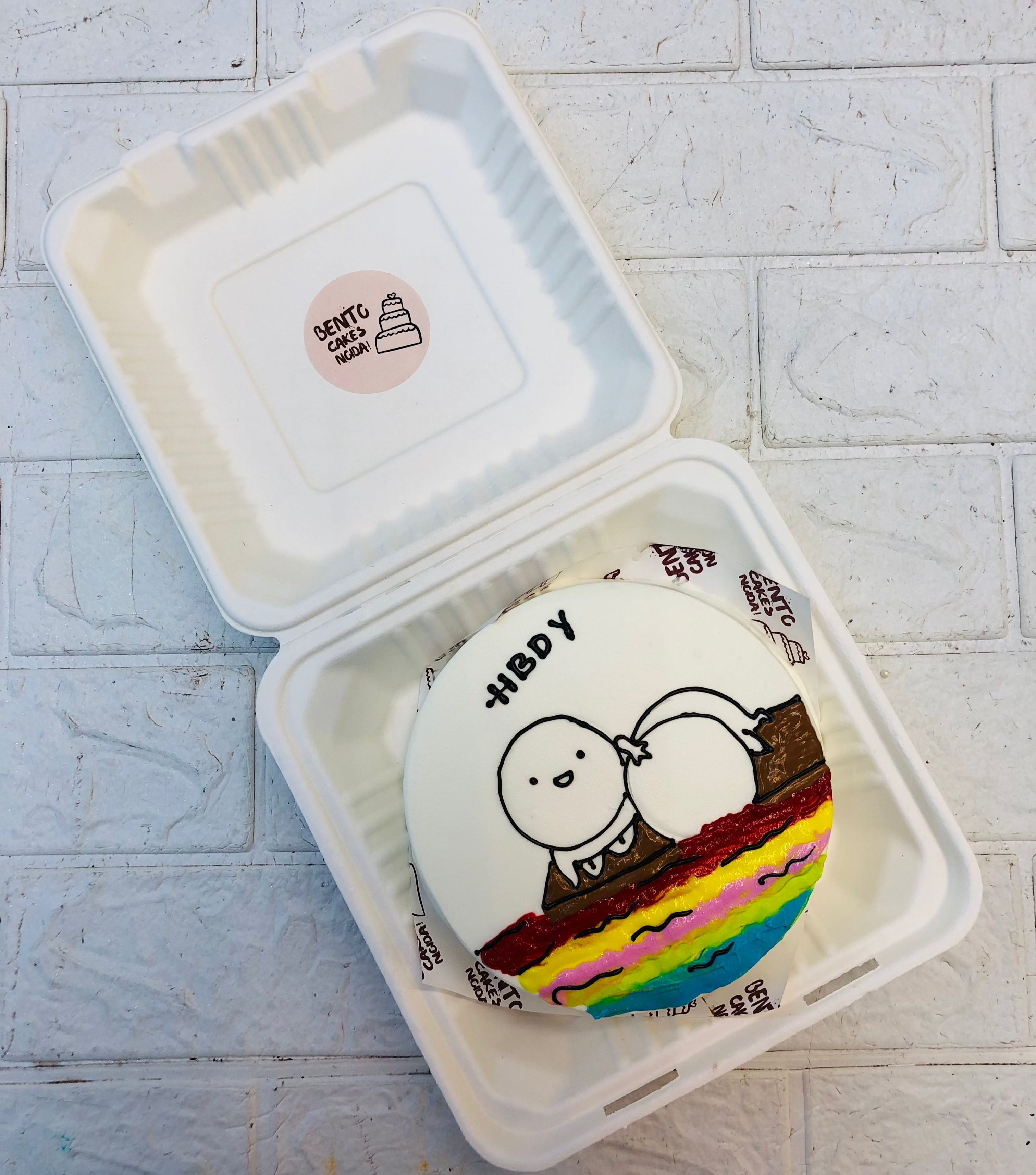 A white bento cake having a sleepy cartoon near beach with colorful wavey design.