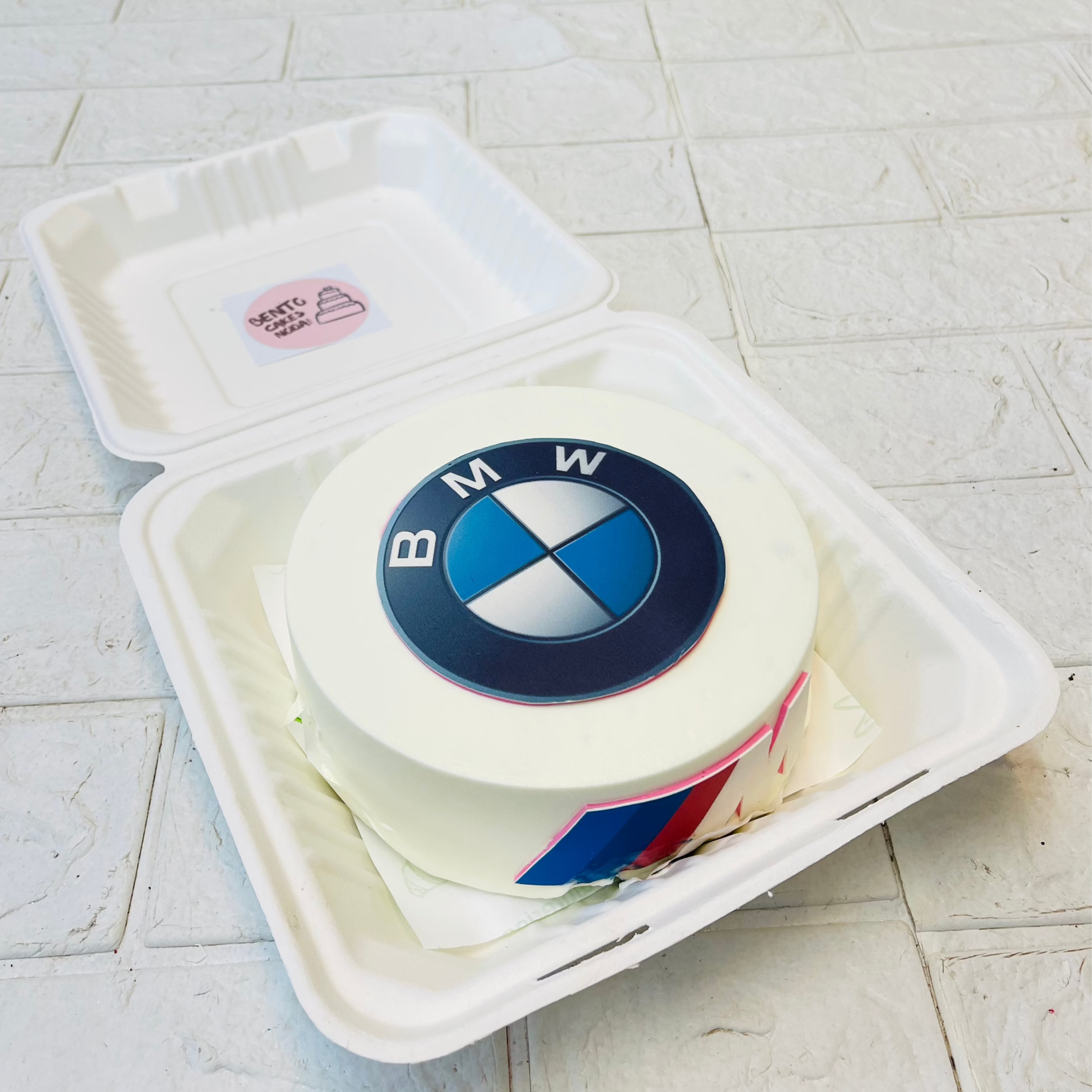 A white bento cake with BMW Car logo print on it.