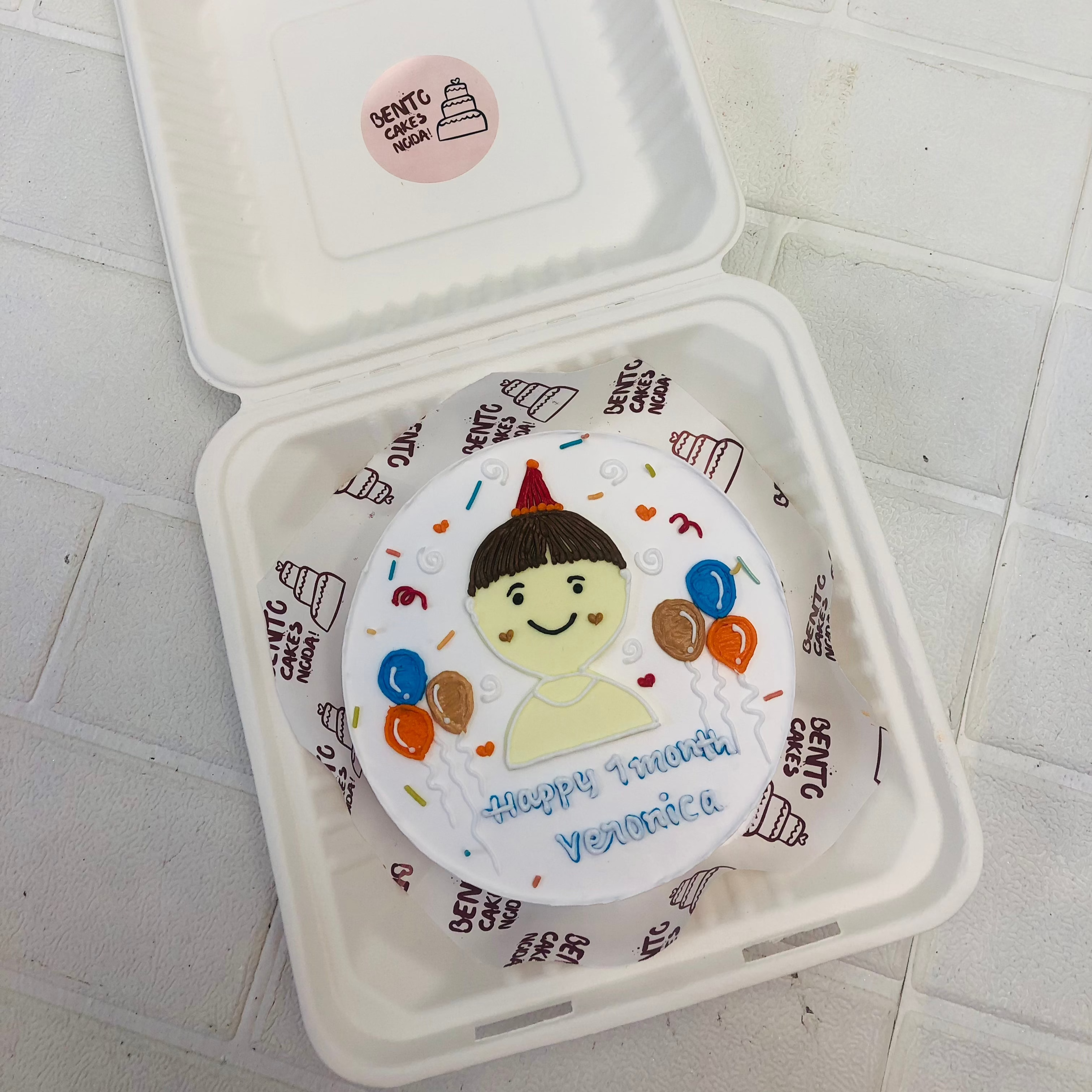 A white bento cake having a cartoon boy's face made and balloons design on cake.